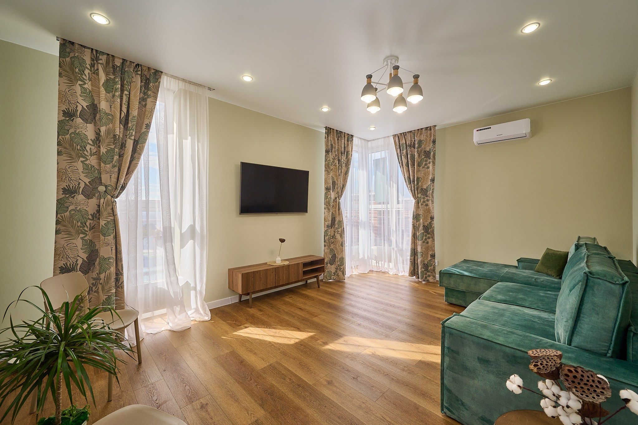 комната зеленый диван коричневый пол коричневая тумба телевизор цветные шторы светлые стены