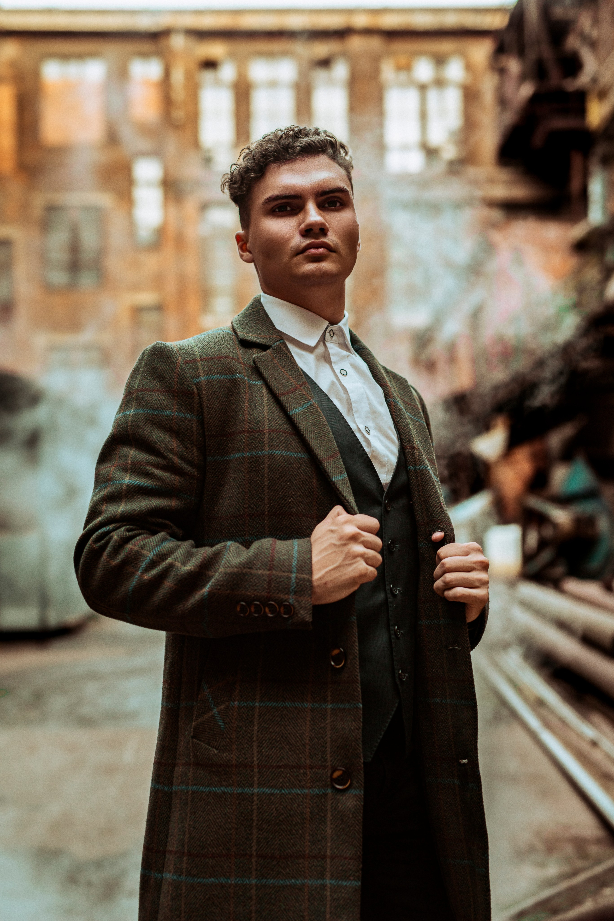 Молодой человек стоит в пальто держась руками за грудки на фоне дыма из труб