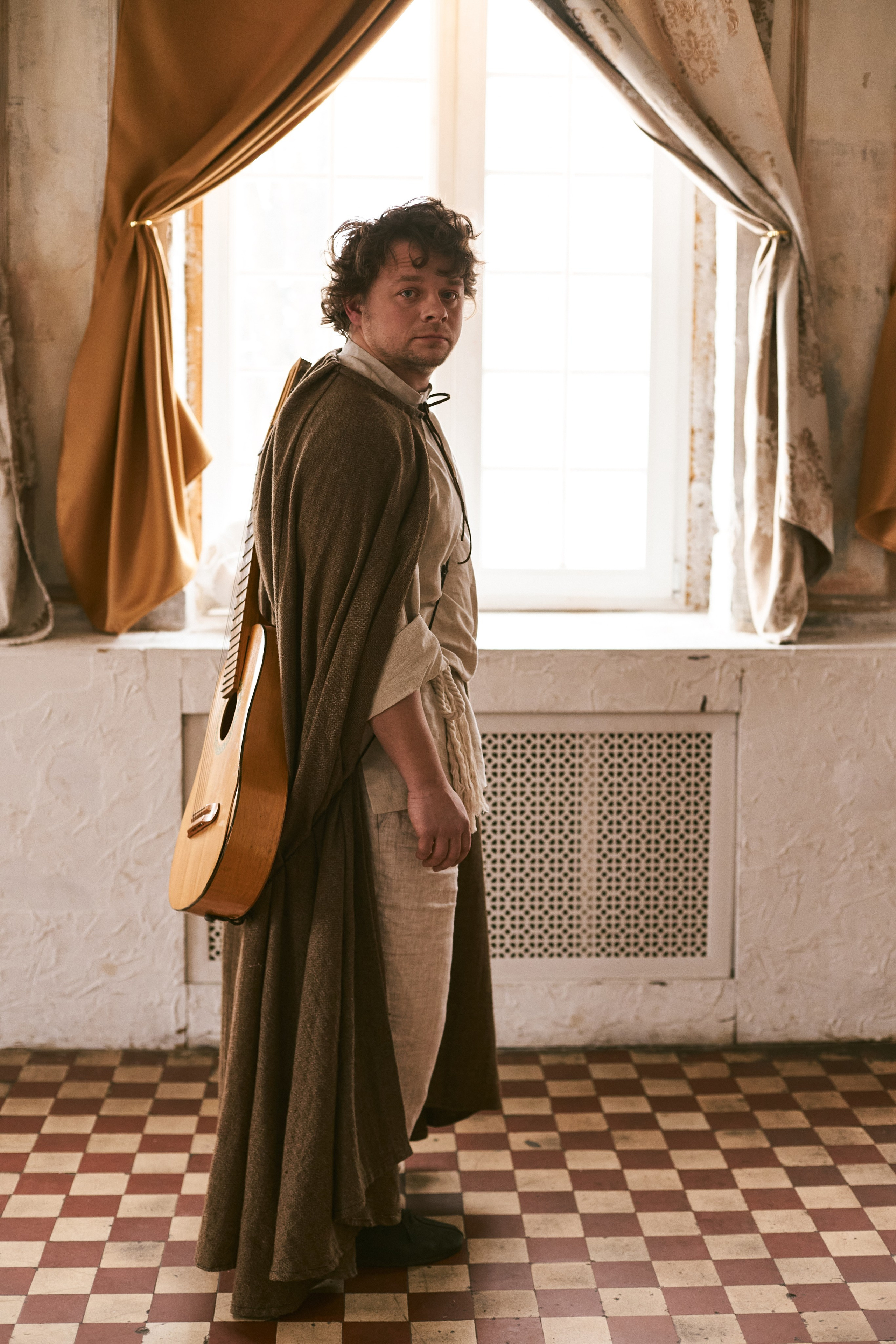 Потрет мужчины с гитарой на спине и в плаще путника в полный рост