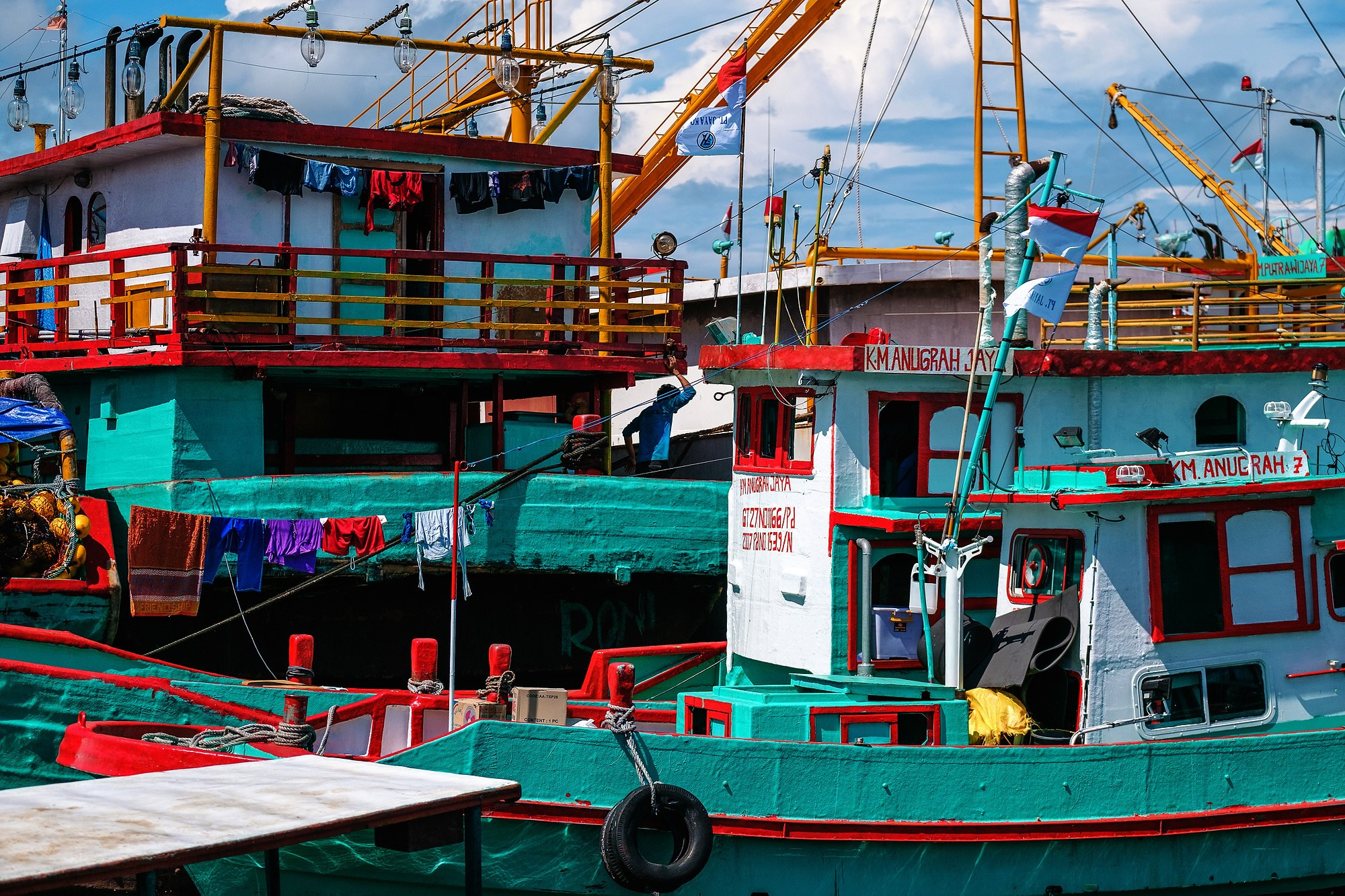 Яркие рыболовецкие корабли зеленого и красного цвета в порту, на палубе сушится одежда на веревке. Документальная и жанровая фотография, насыщенные цвета, портовый быт. Автор Виктор Молодцов.