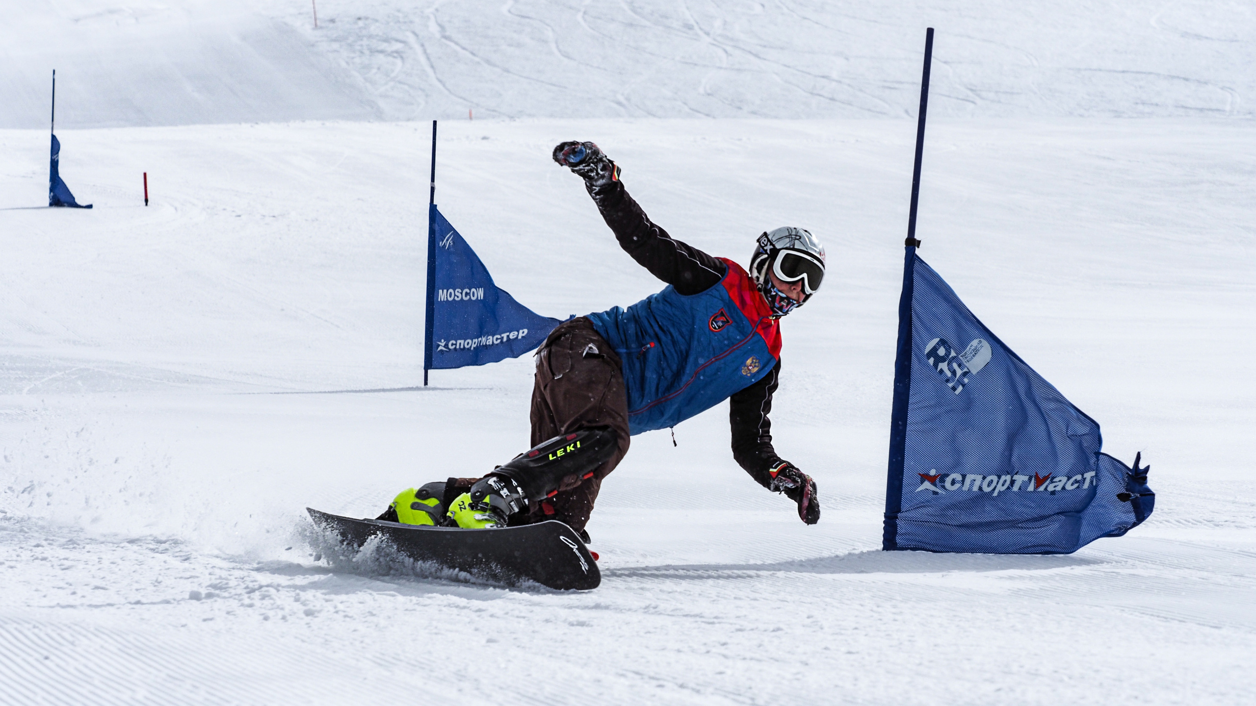 Спортсмен- сноубордист на скорости объезжает флажок на снежном склоне