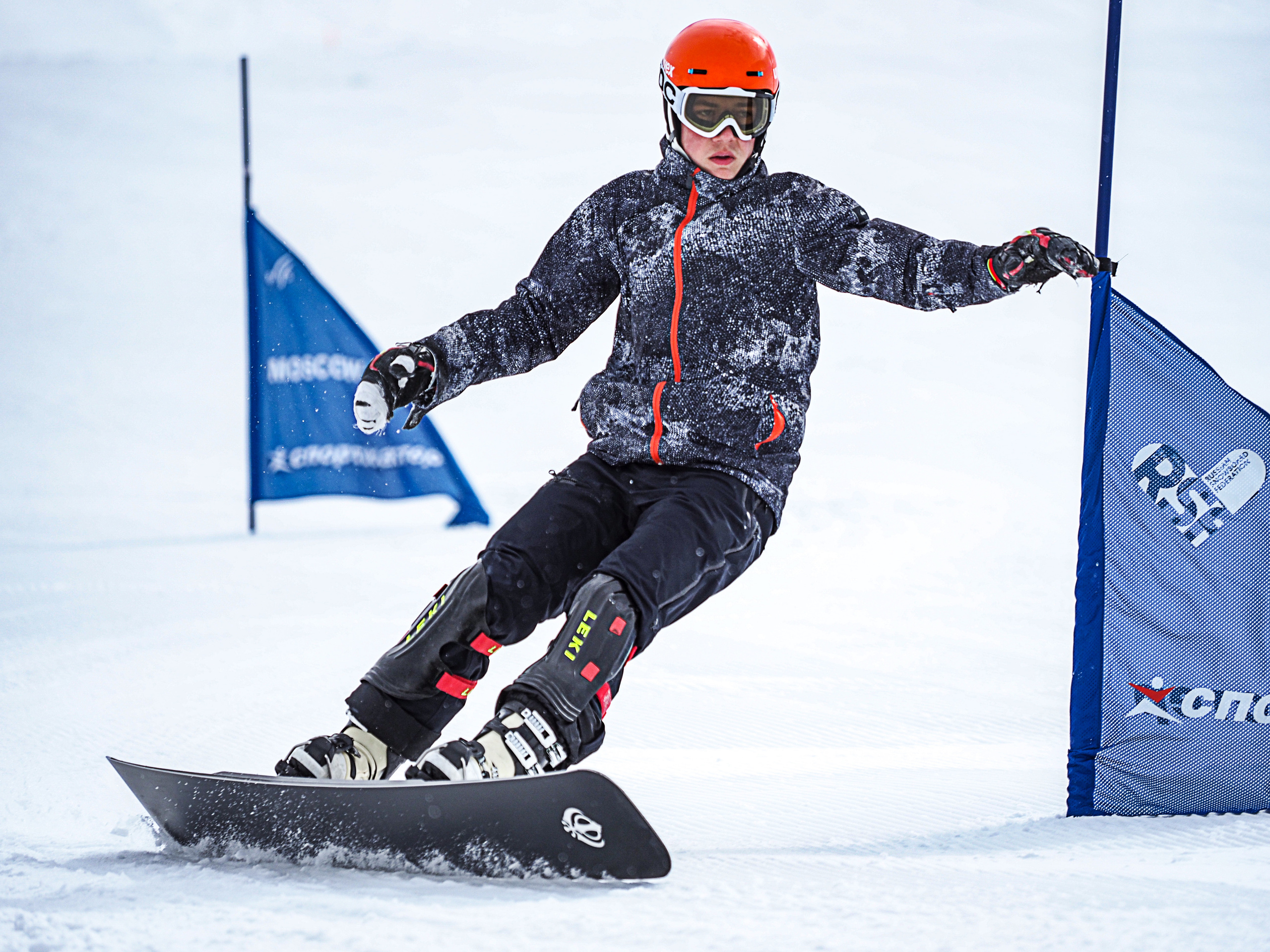 Спортсмен- сноубордист , слалом, на скорости объезжает флажок на снежном склоне