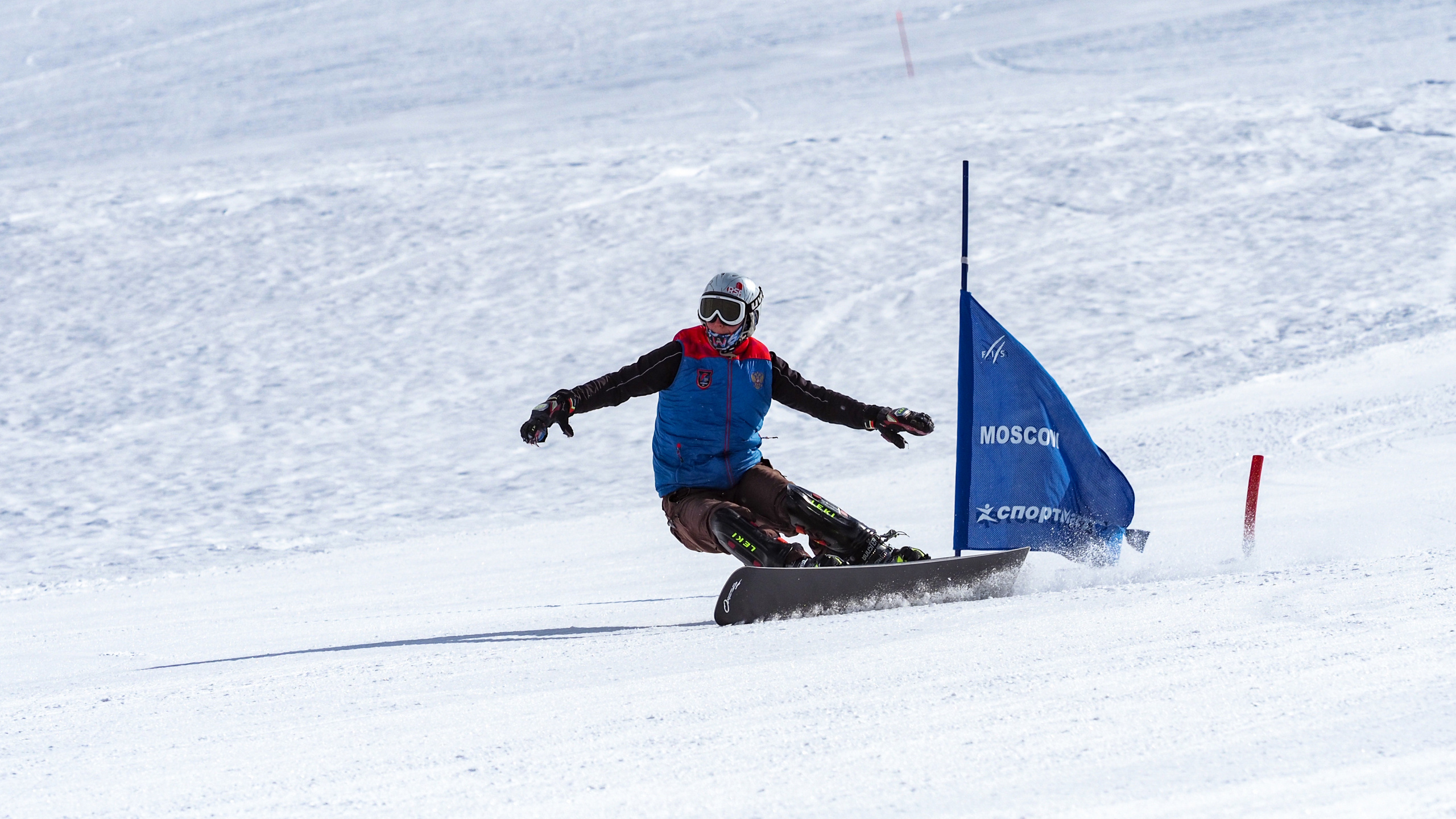 Спортсмен- сноубордист на скорости объезжает флажок на снежном склоне