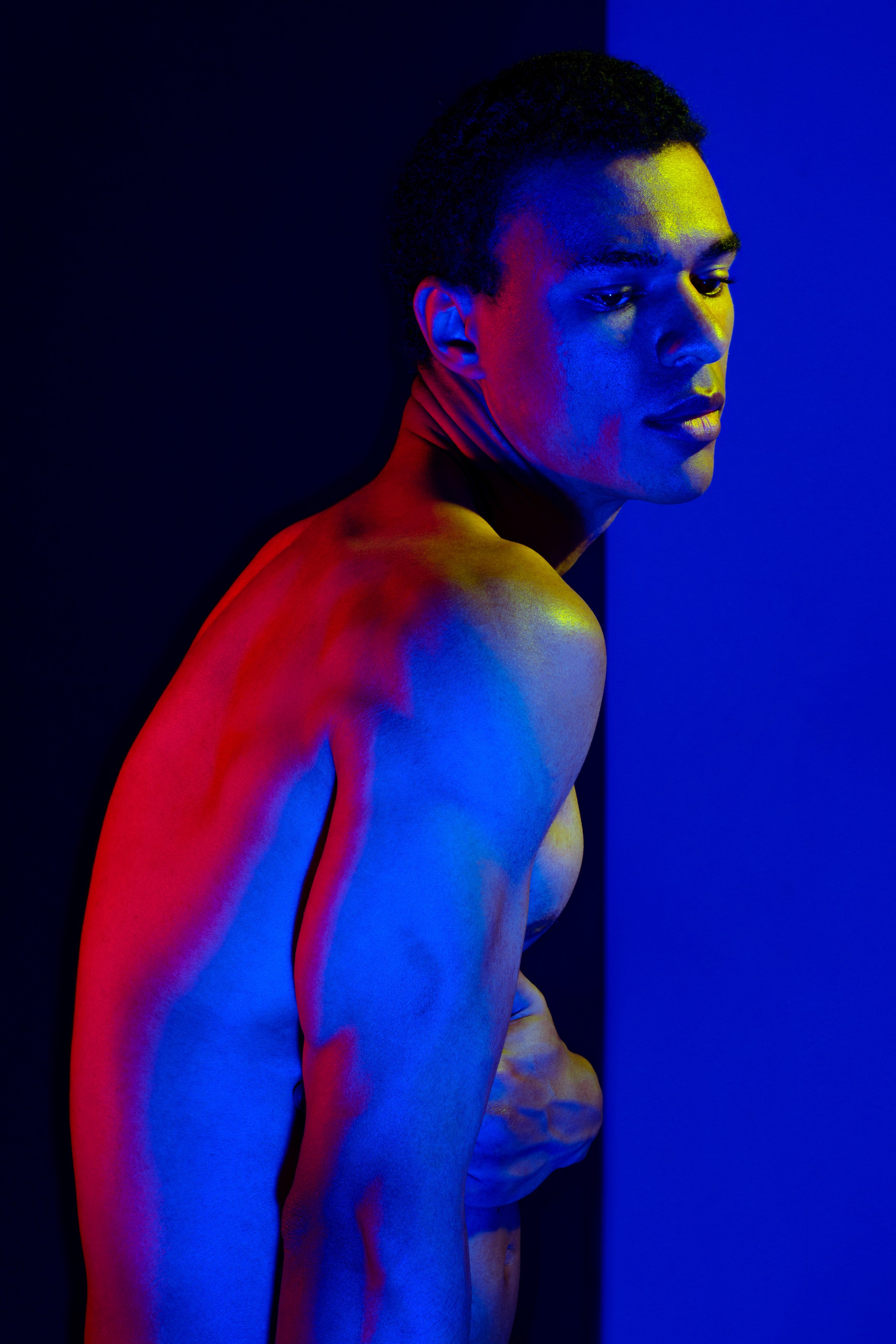 чернокожий обнаженный мужчина на черном фоне в цветном свете 