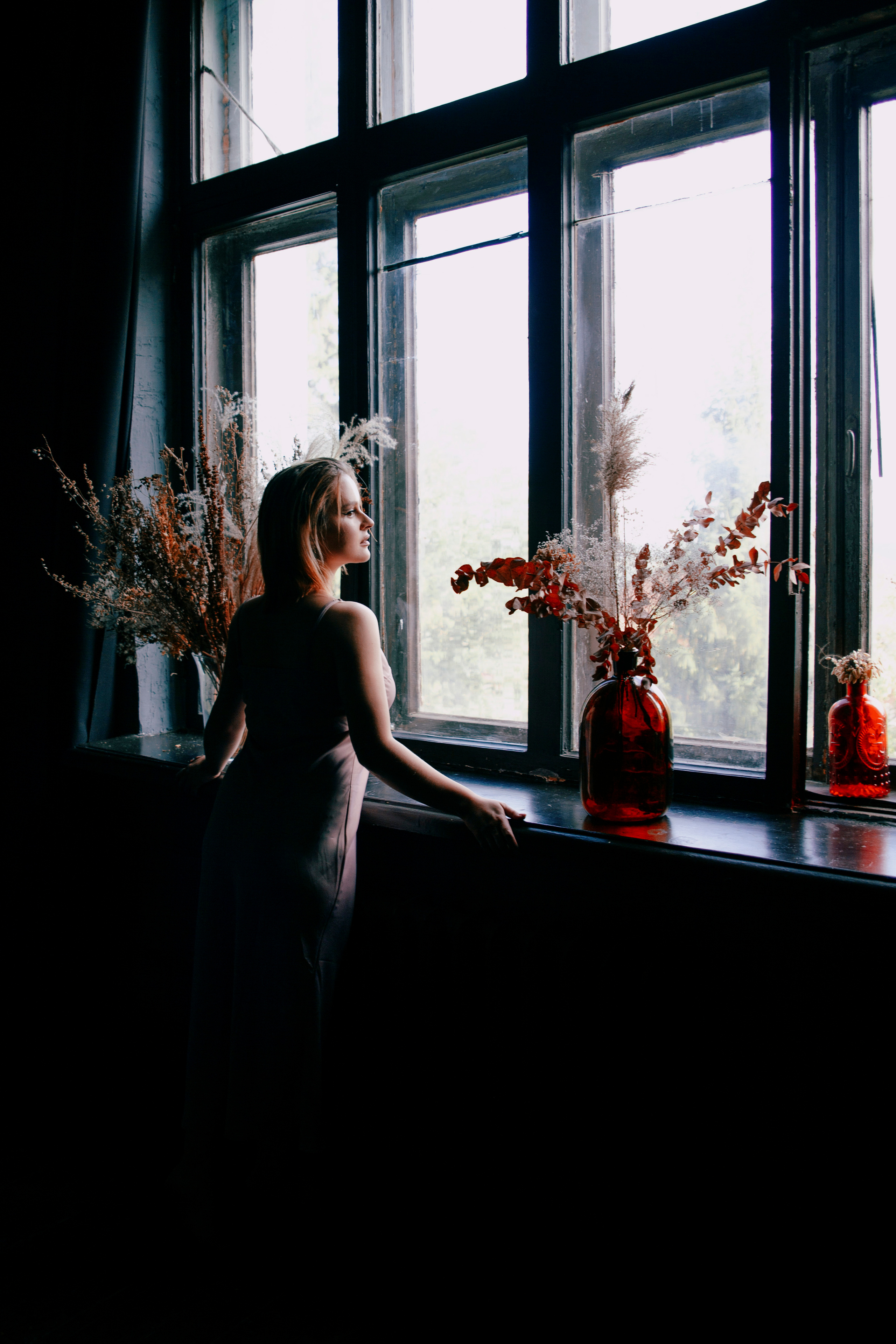 Силуэт девушки у окна на фоне цветов.