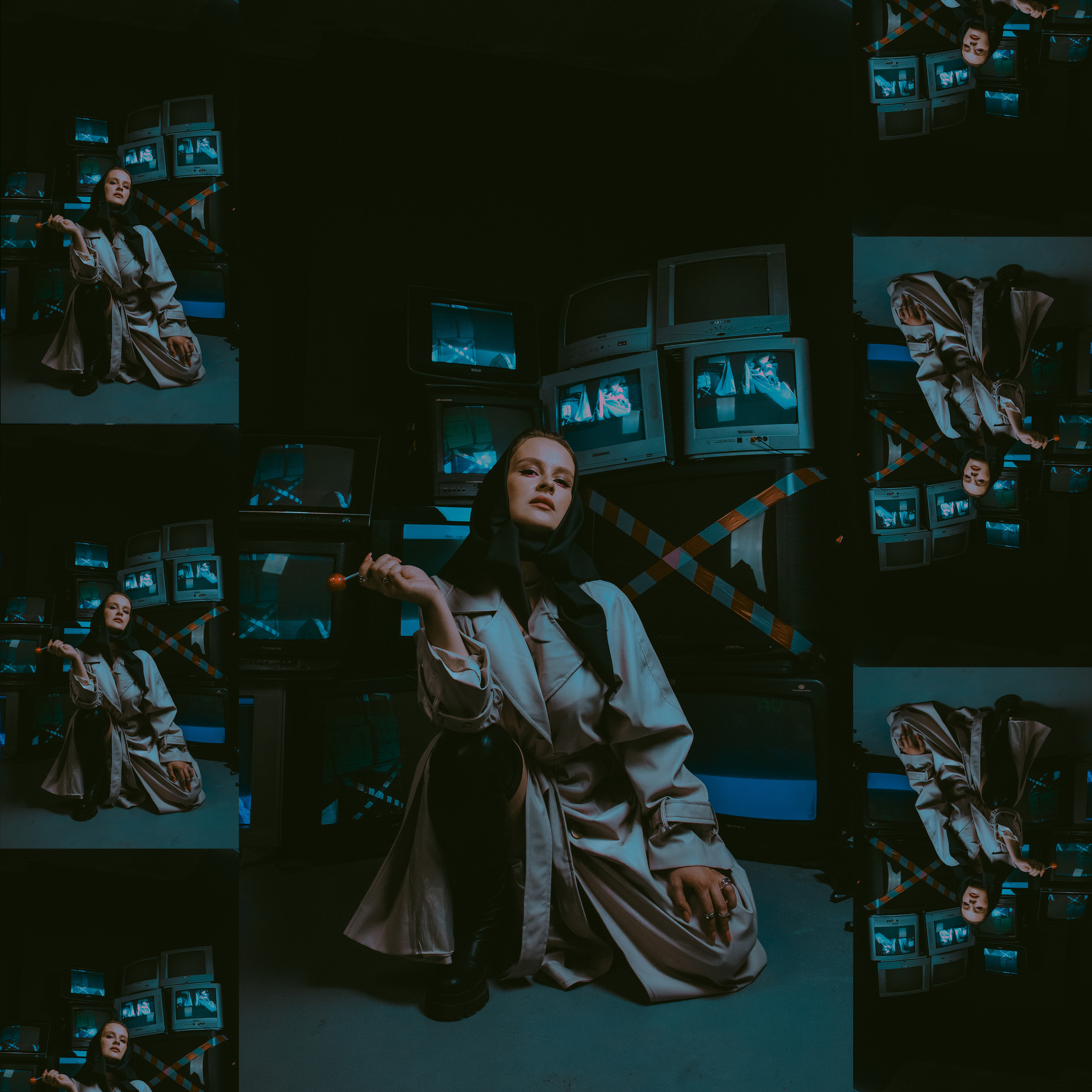 Девушка в плаще и кожаной косынке сидит на фоне старых телевизоров.