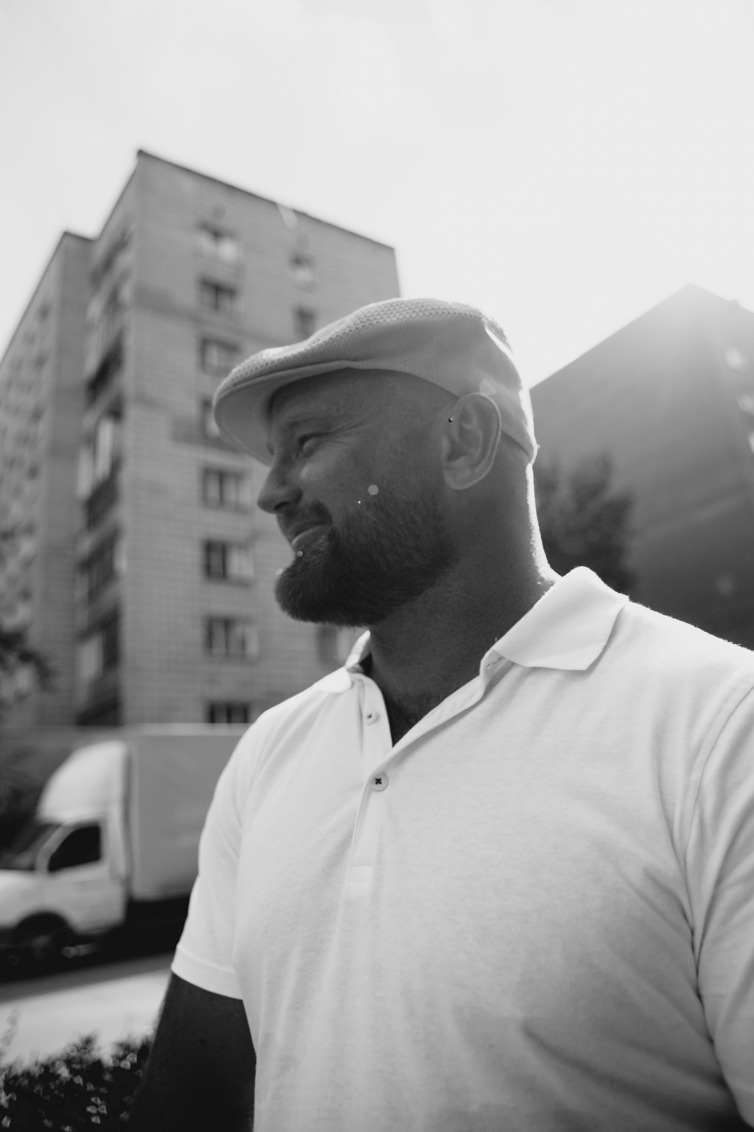 Черно-белый портрет мужчины в кепке и белой футболке поло.