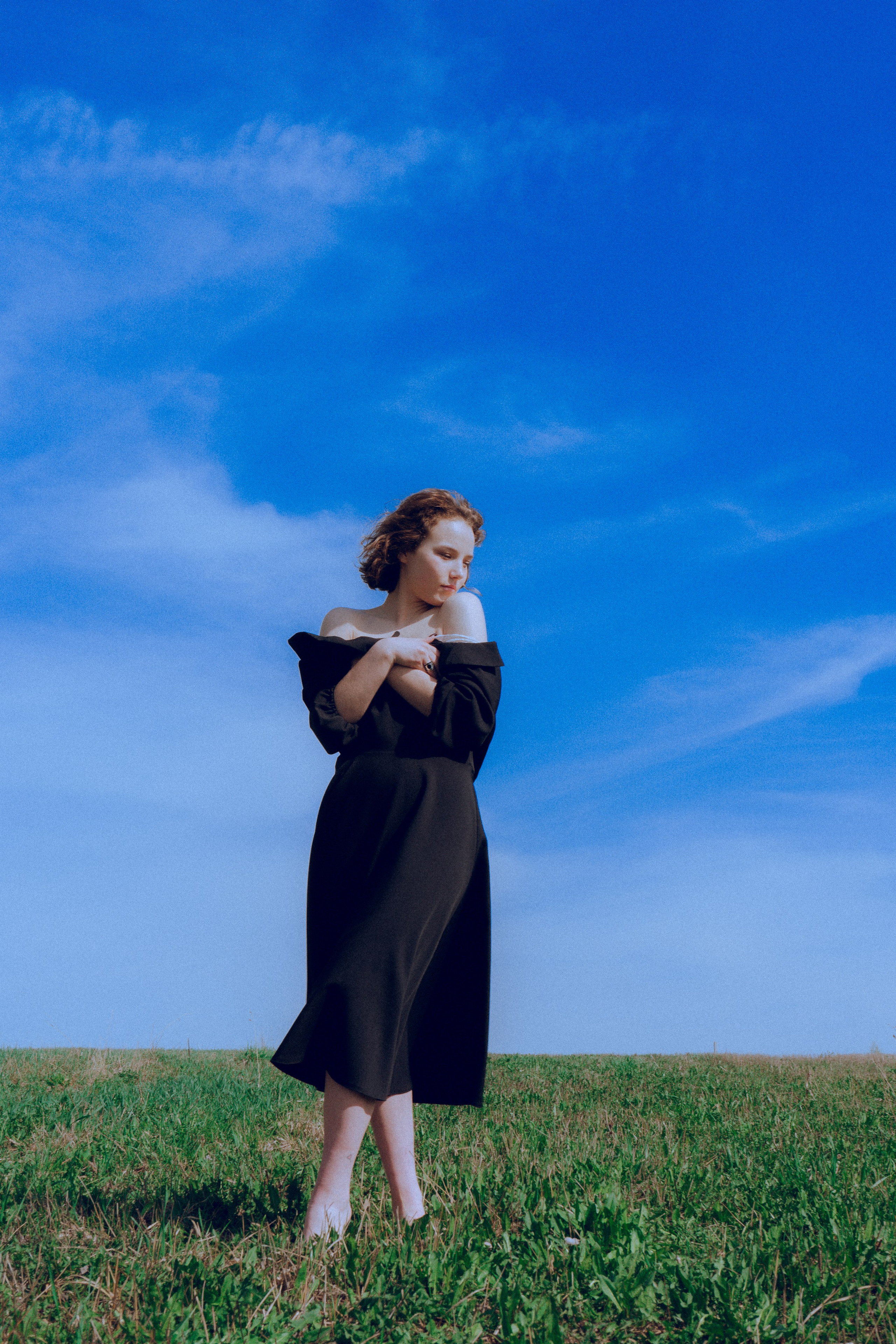Девушка в чёрном платье позирует в поле