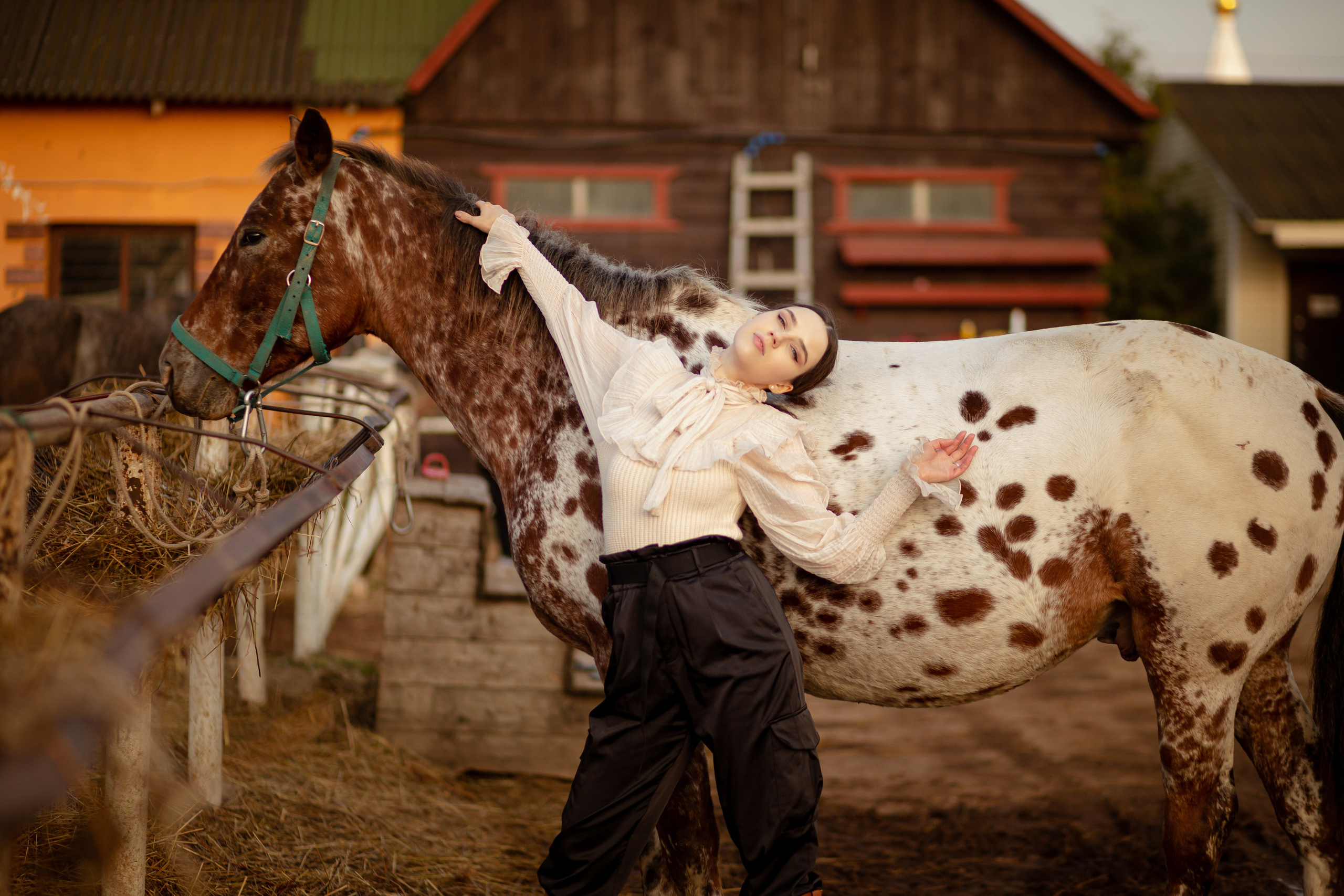 Девушка на фоне дома стоит возле лошади.