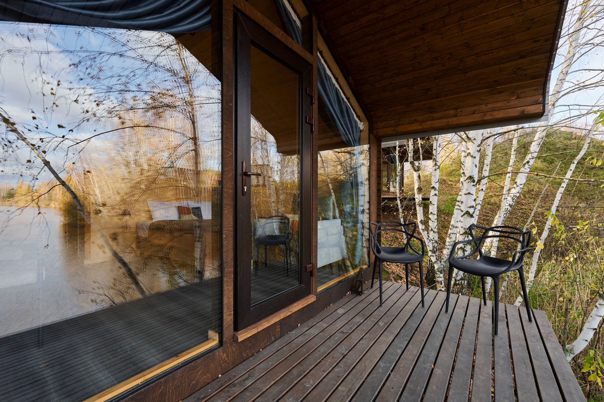 Крытая веранда, кресла и вид на реку сквозь деревья.