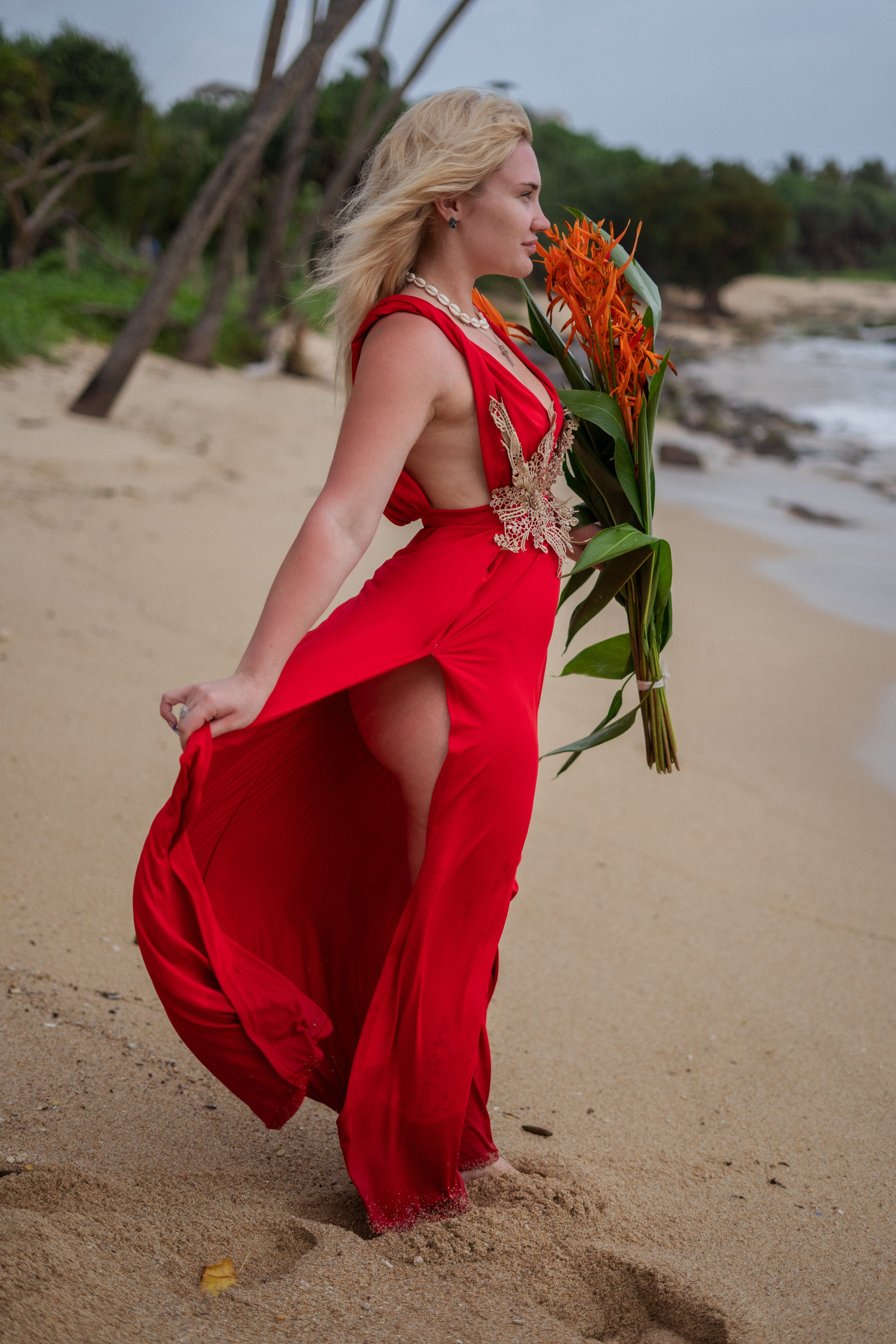 a beautiful blonde in a red dress walking along the beach by the ocean