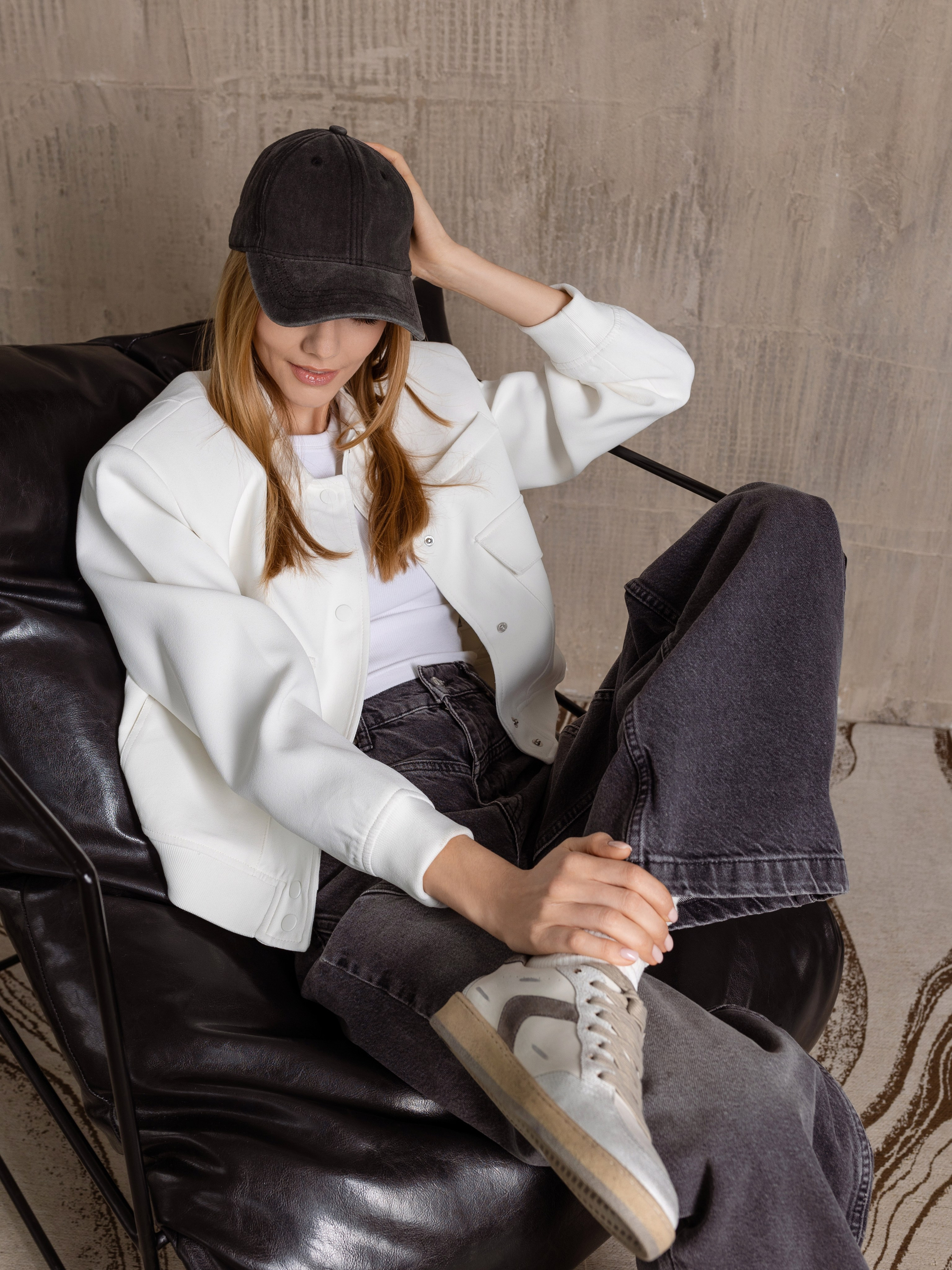 Сидящая на кресле девушка придерживает на голове черный кепи.