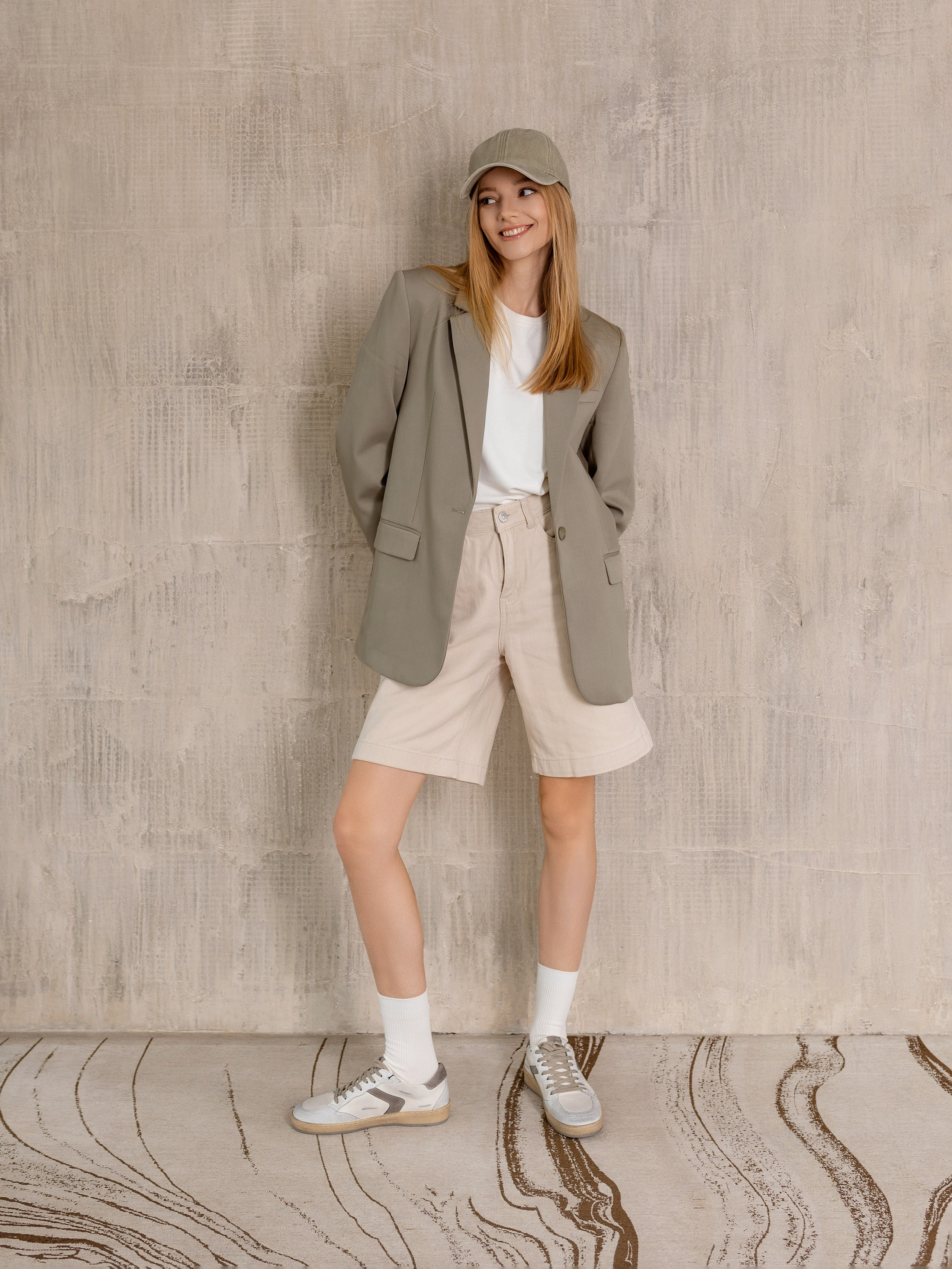 Девушка фоне серой стены и на голове серый кепи.