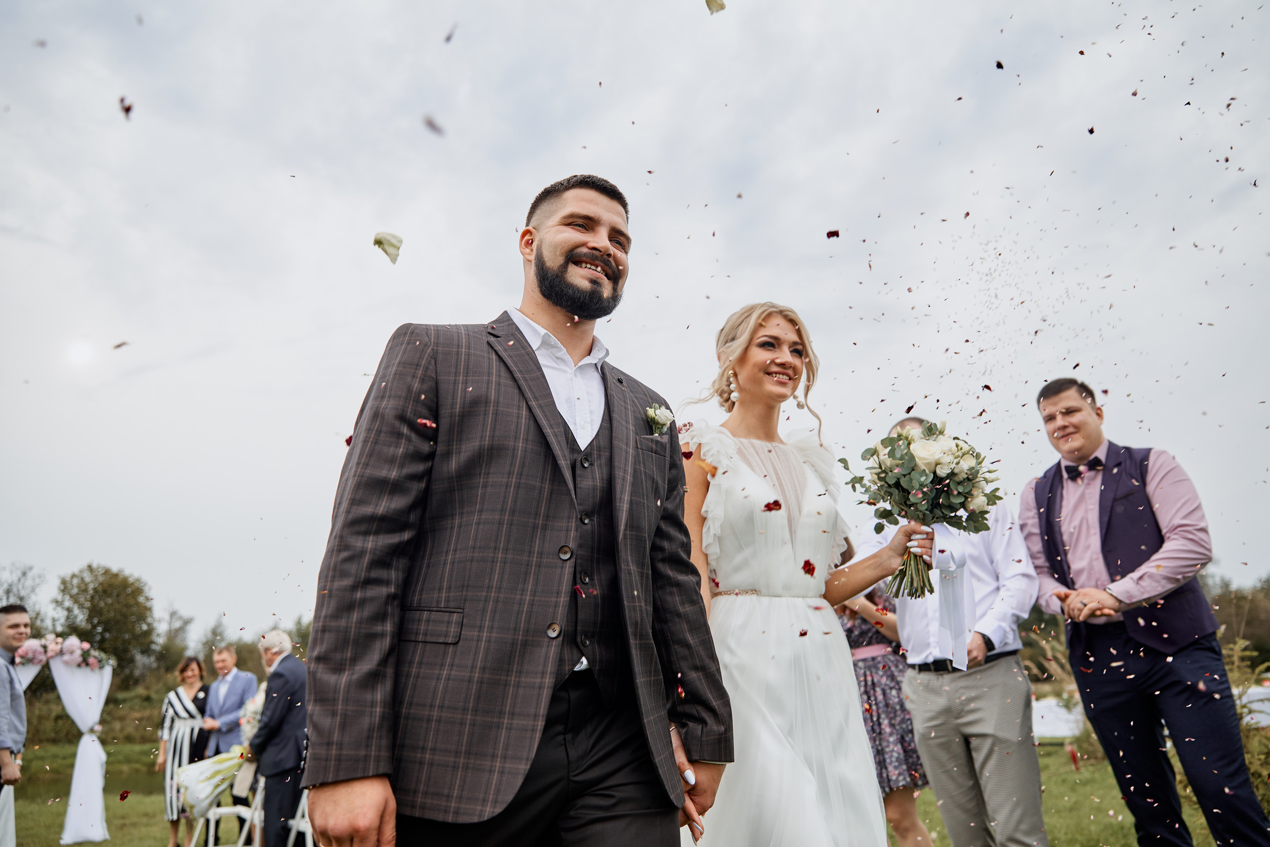 счастливый жених и невеста идет под лепестками роз 