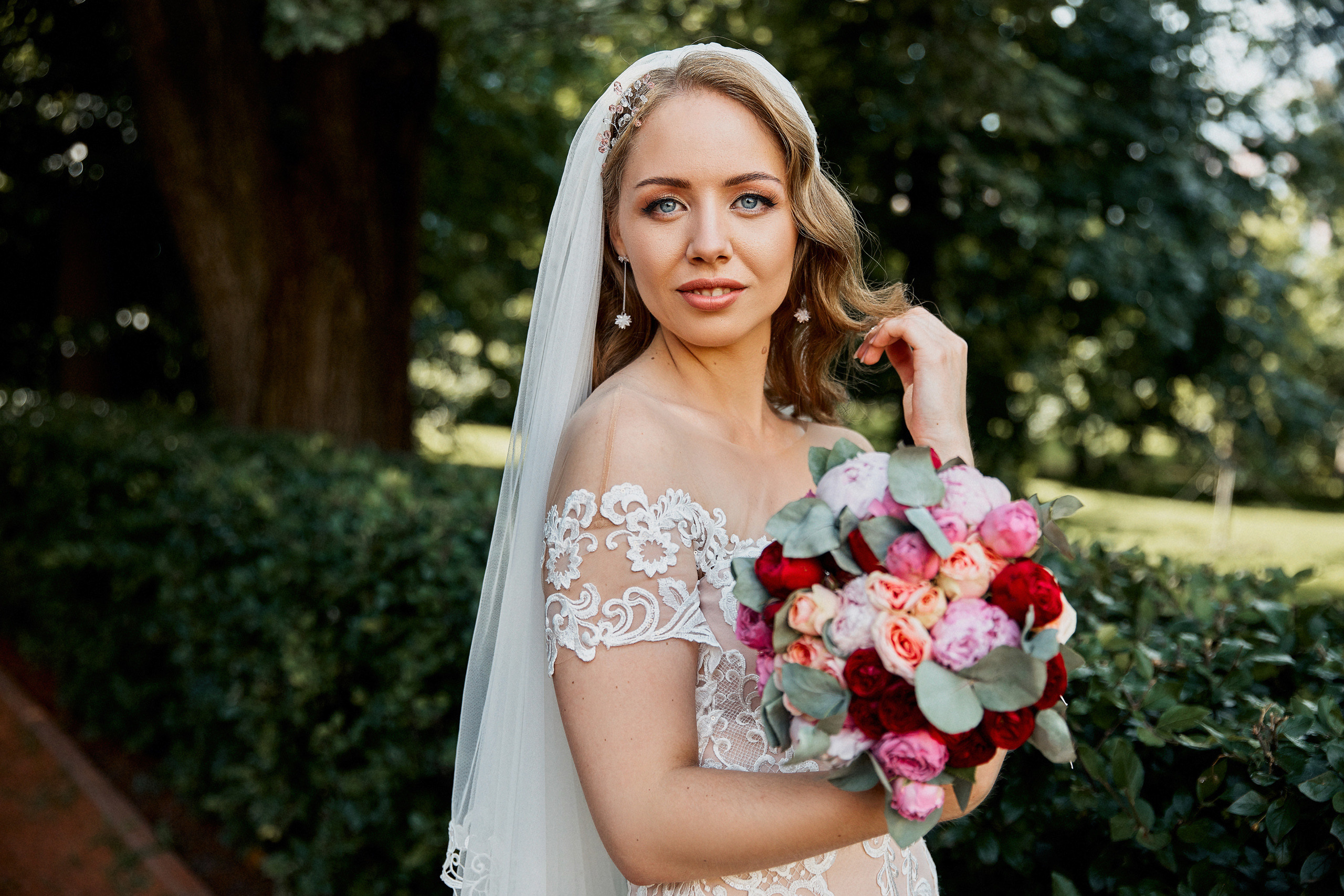 невеста смотрит нежным взглядом теребя свои волосы и держа красивый букет