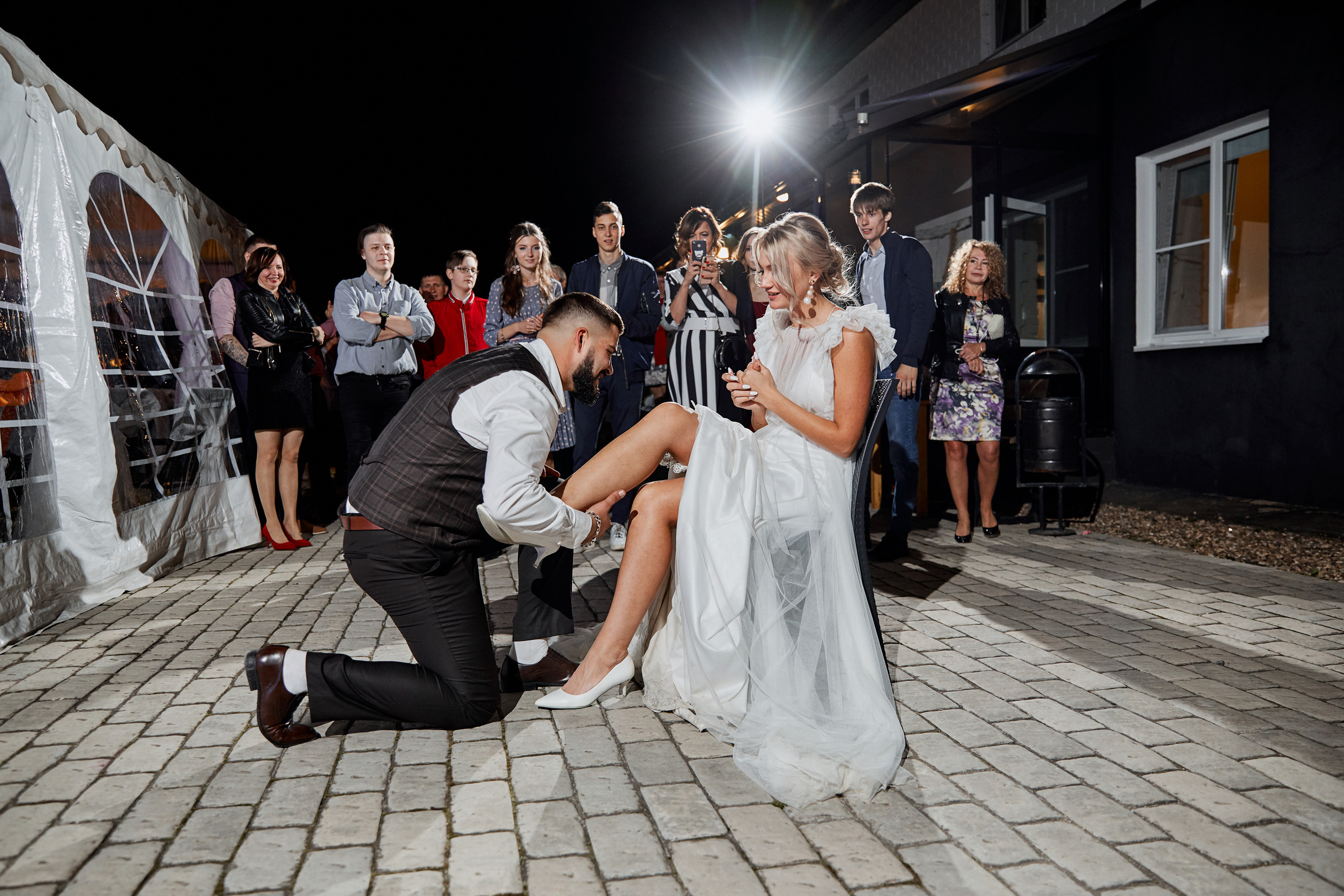 жених снимает подвязку с ноги невесты стоя на колене