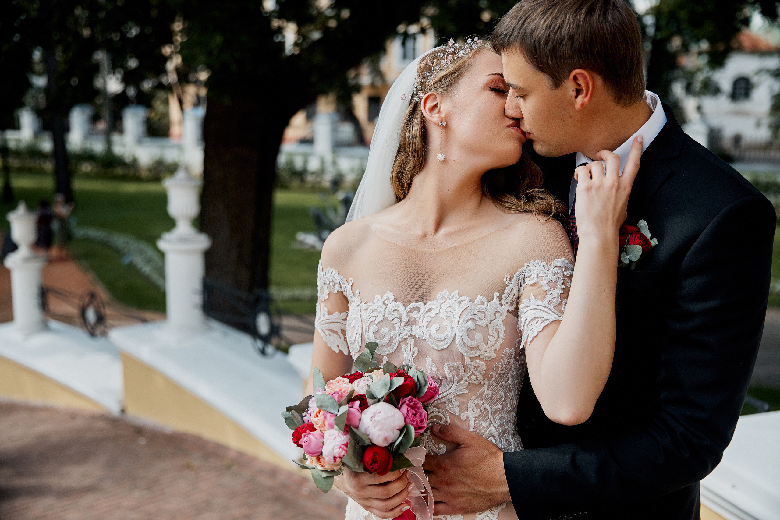 молодожёны целуются, жених держит невесту за талию, а она проводит по его щеке ладошкой