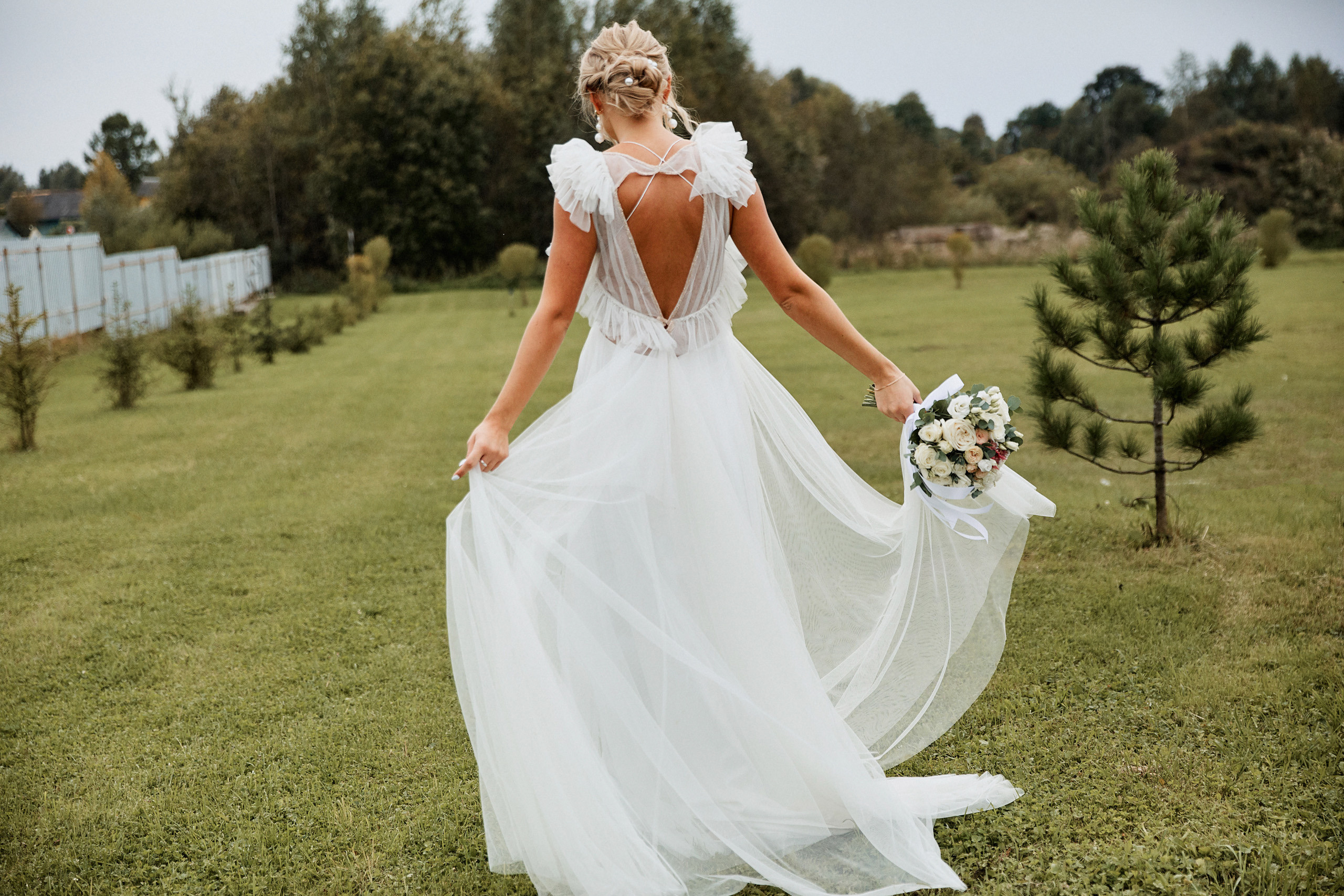 Невеста показывает свое красивое платье стоя спиной к фотографу 