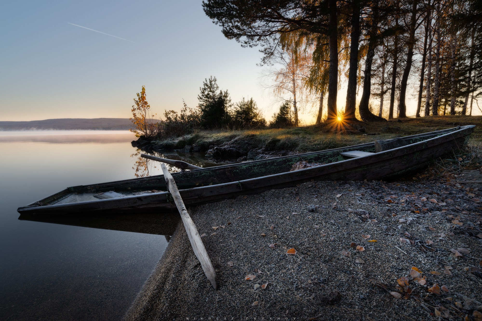 Осенний пейзаж со старой лодкой, покрытой инеем, солнце светил сквозь деревья.