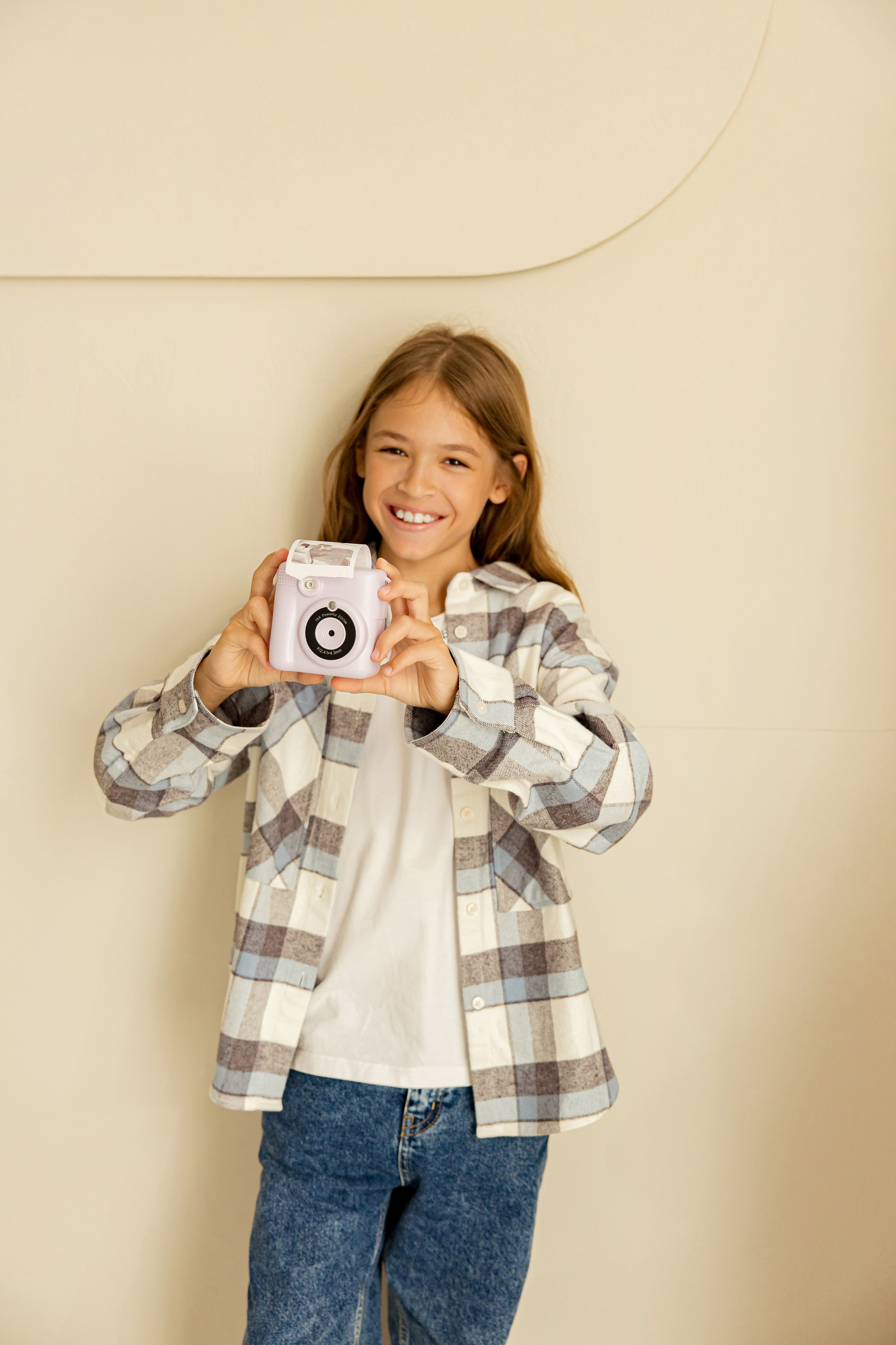 Девочка в рубашке весело фотографирует на камеру моментальной печати