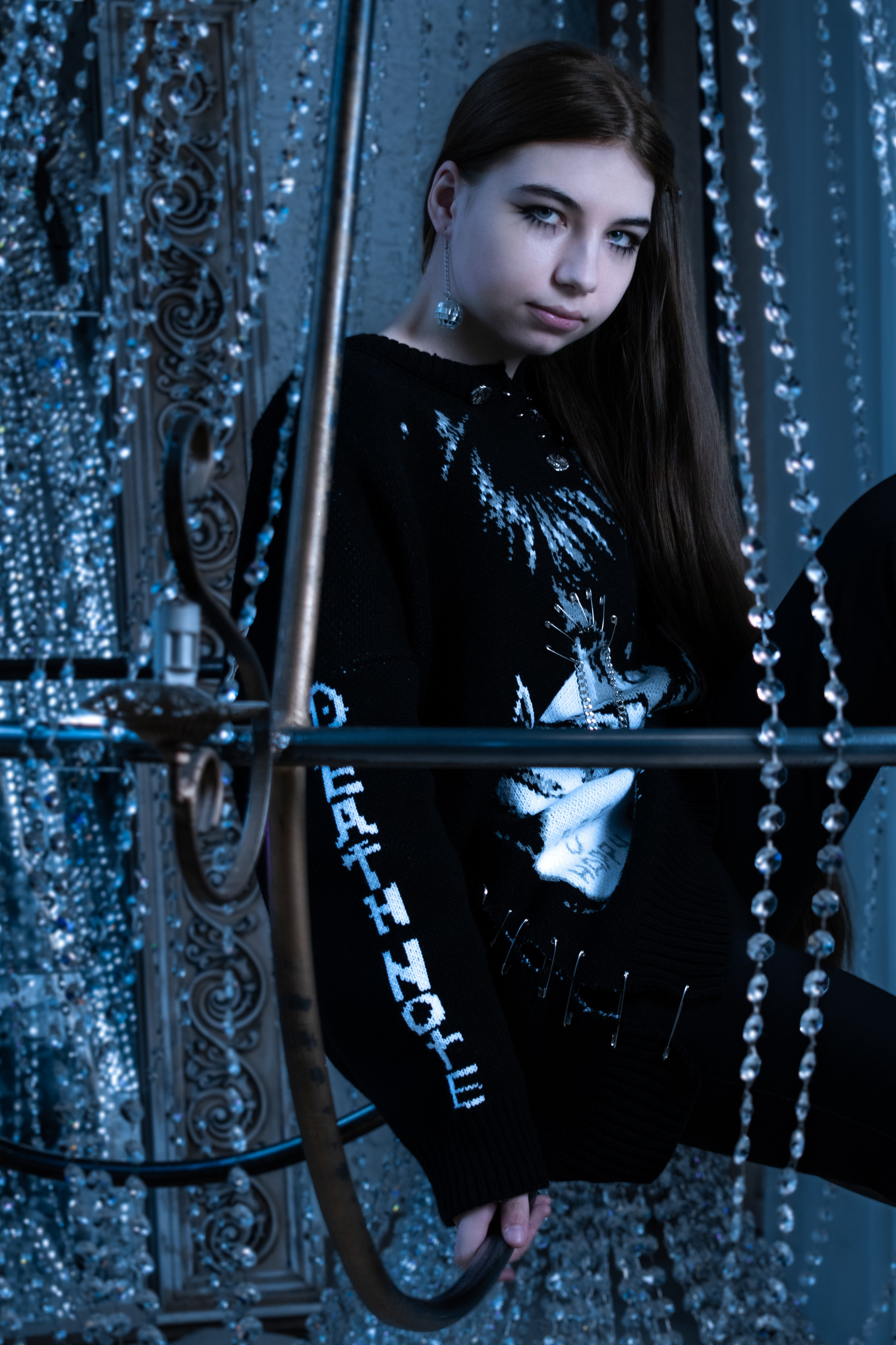 Девушка с длинными волосами в черном свитере сидит в хрустальной люстре