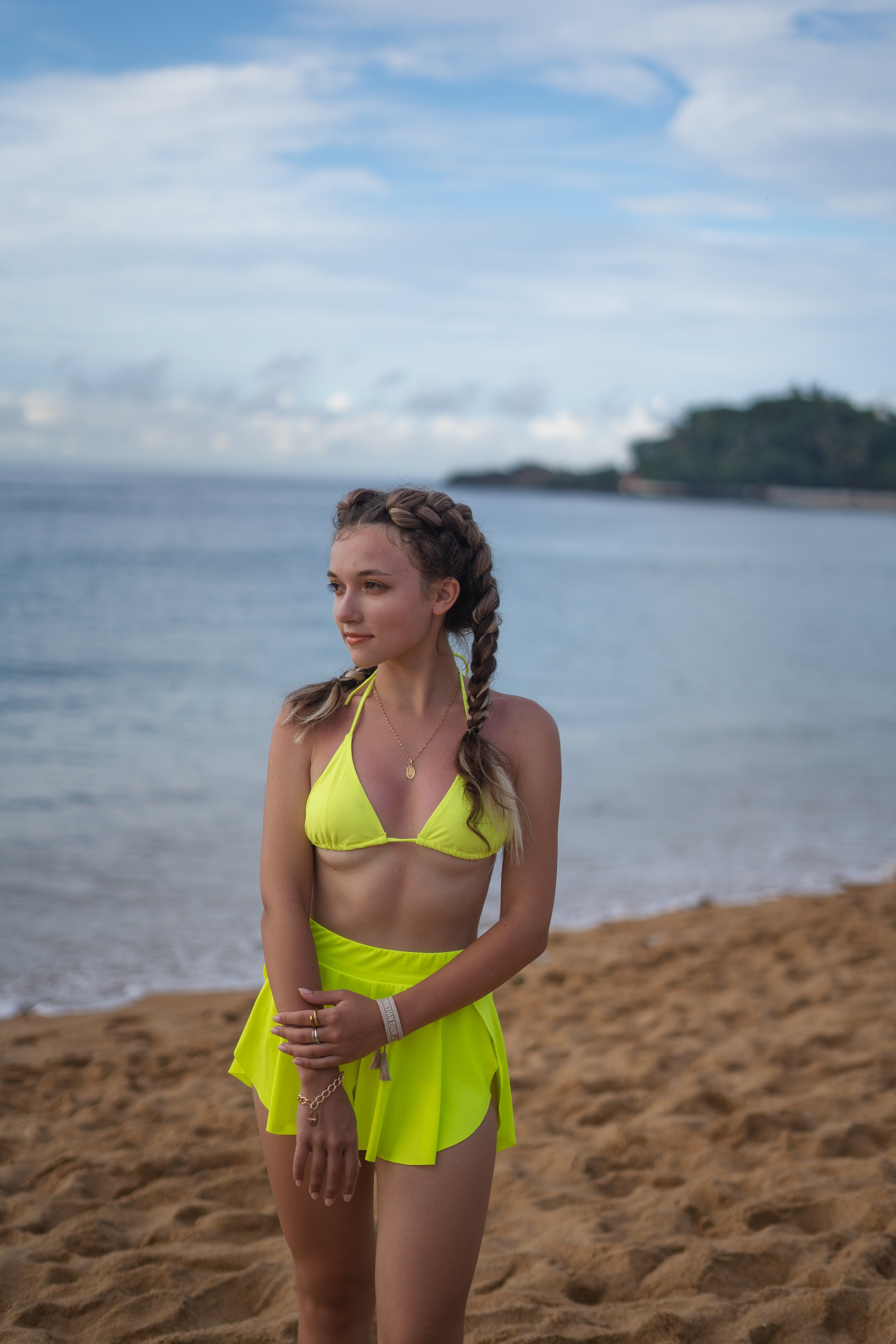 a girl with braids in a yellow swimsuit sitting on the sand by the ocean
