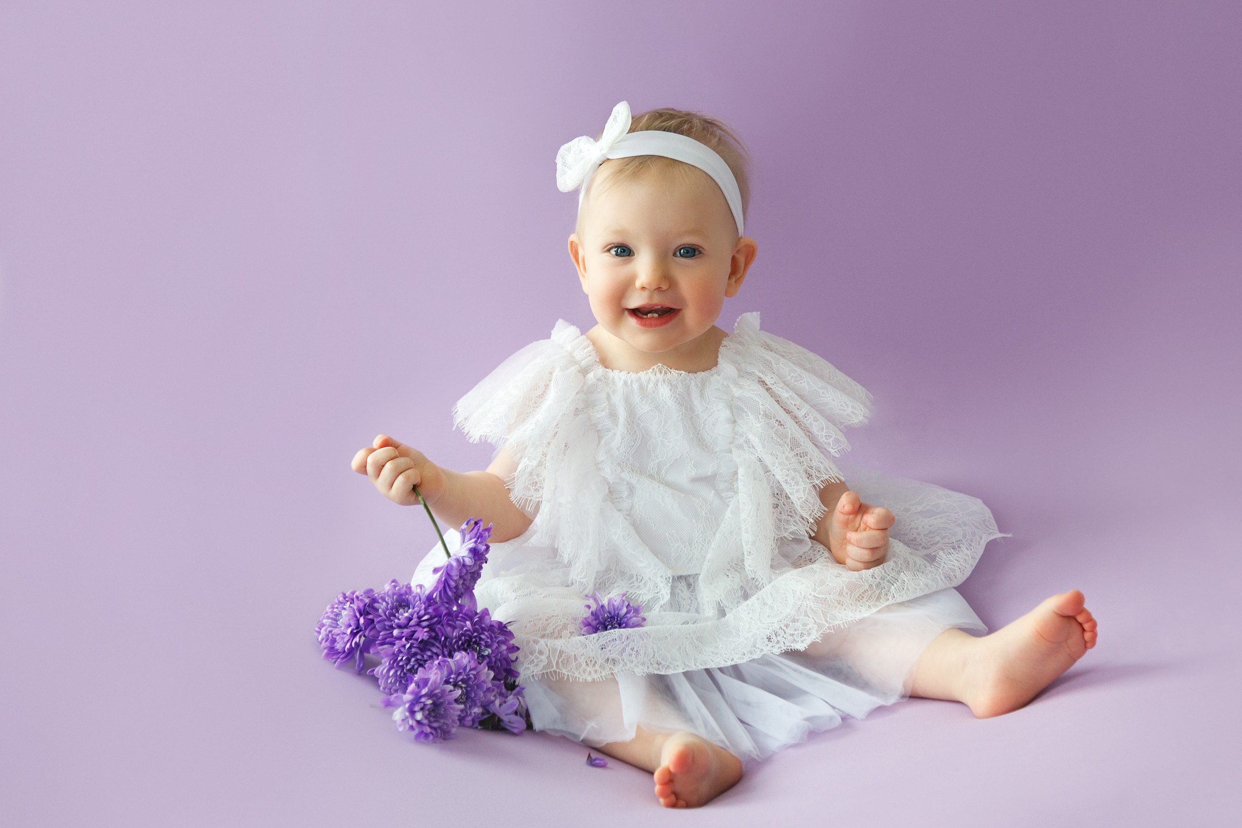 малышка с цветами на сиреневом фоне в белом кружевном платье
