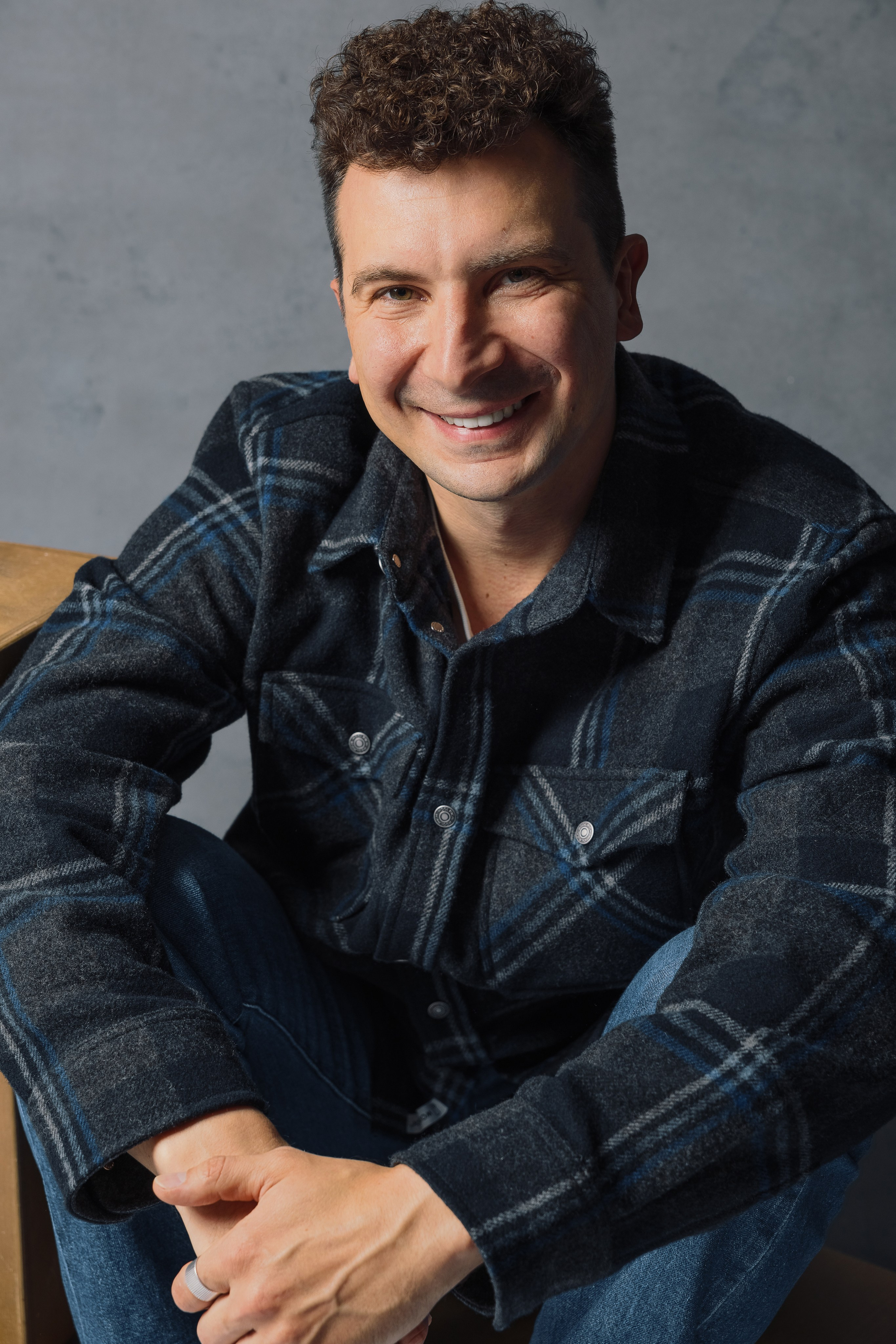 Портретная фотография мужчины в джинсах и клетчатой рубашке на сером фоне