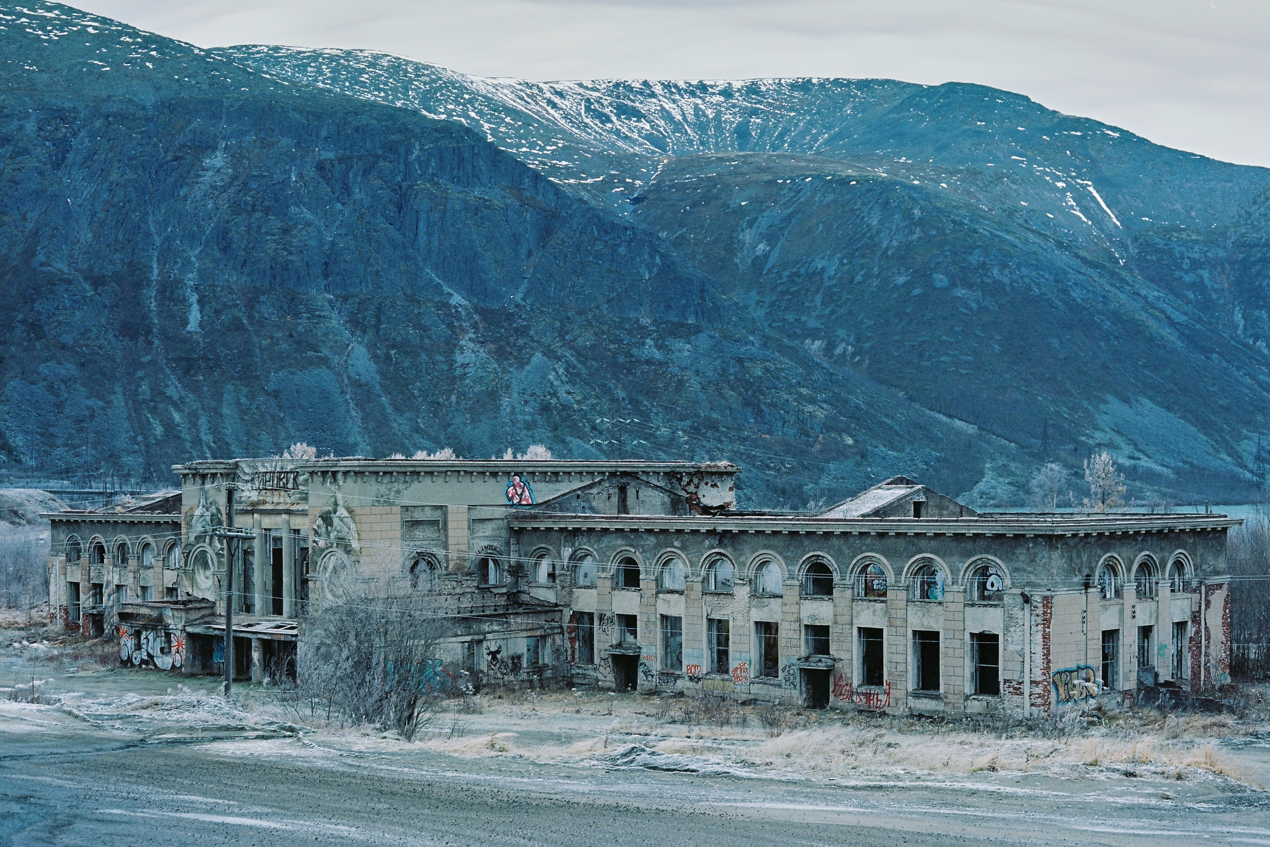 Депрессивный постапокалиптический вид на полуразрушенное здание железнодорожного вокзала слившегося с горой на его фоне в Кировске, Россия.