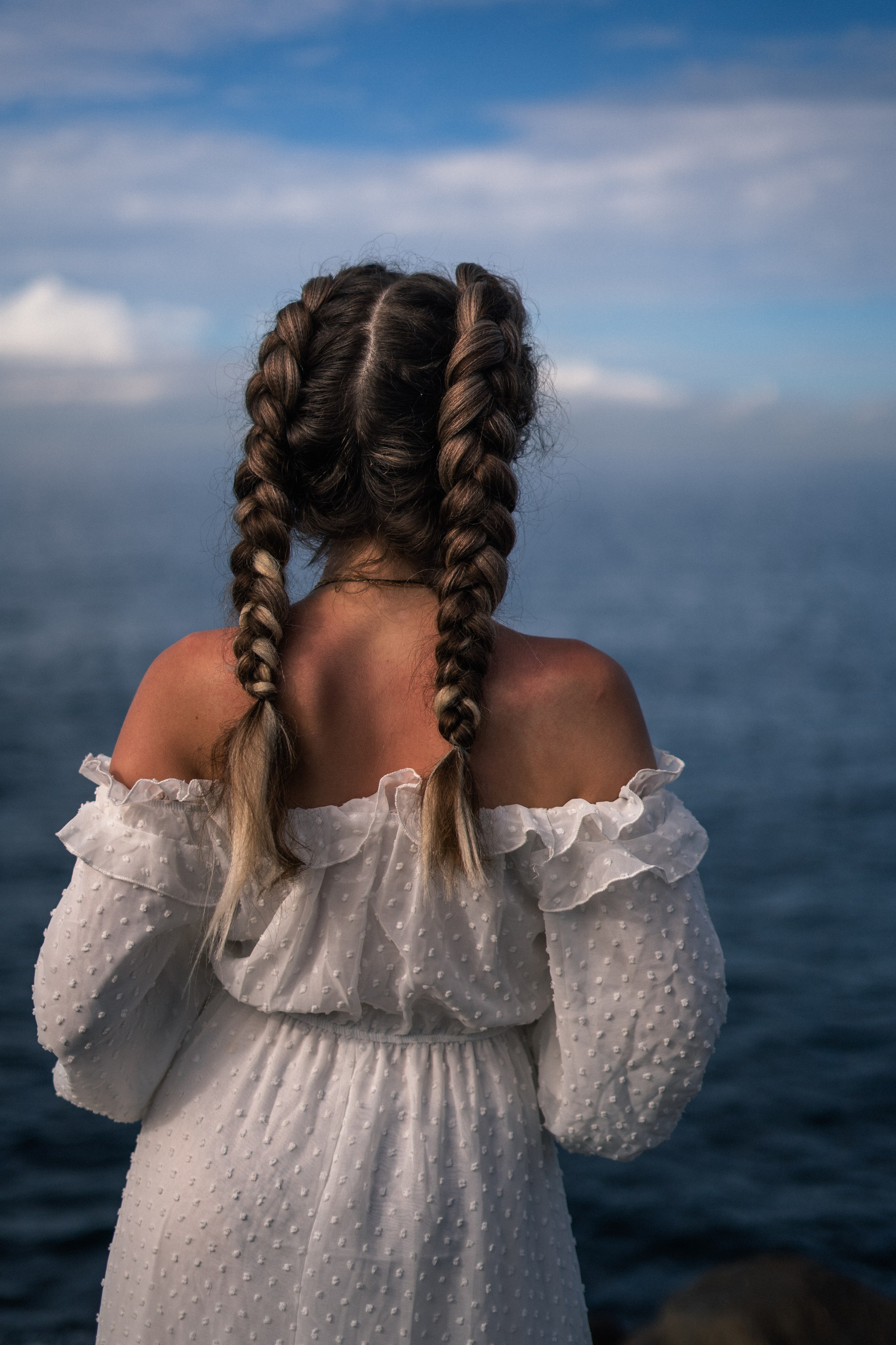 a young beauty in a white dress and glasses on the rocks at the ocean's edge
