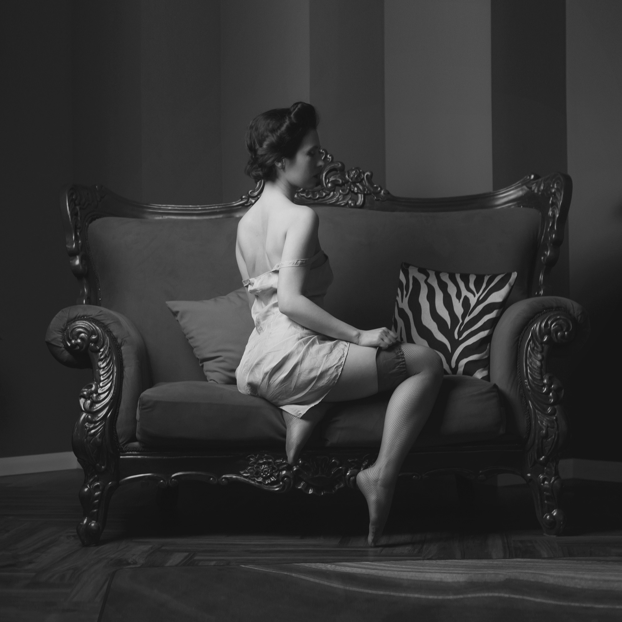 Ретро-съёмка, в черно-белом. Девушка со старинной причёской на диване. Вид со спины.