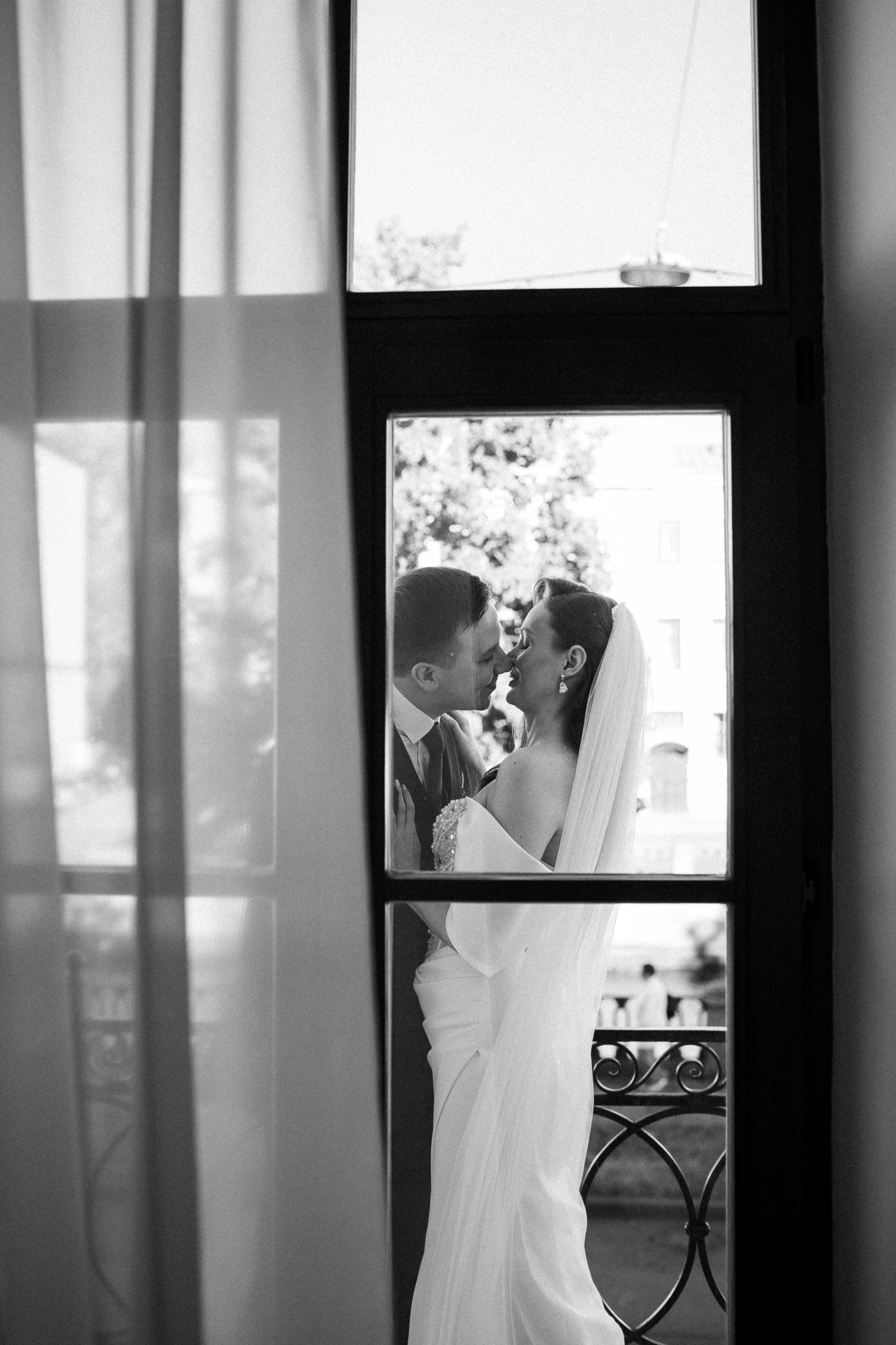 Красивая черно-белая фотография: жених и невеста целуются на балконе отеля.