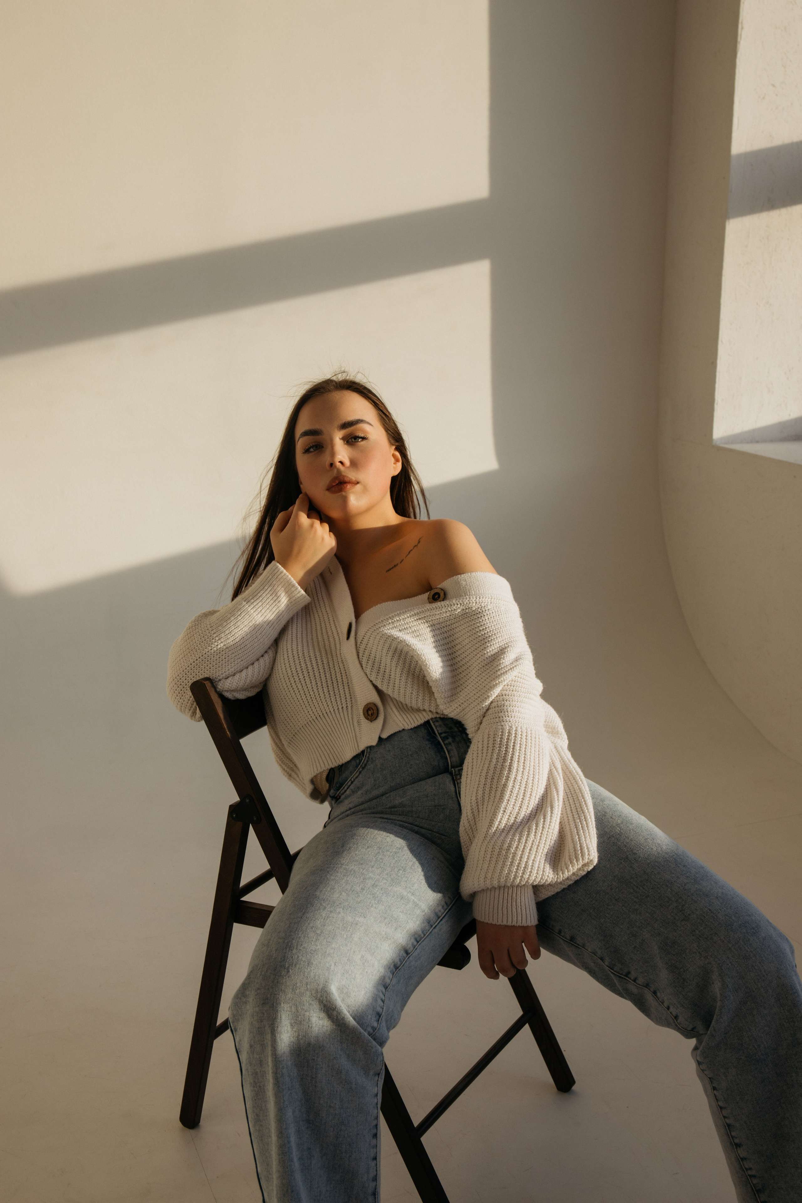 Девушка в светлых оверсайз джинсах и кардигане сидит на стуле
