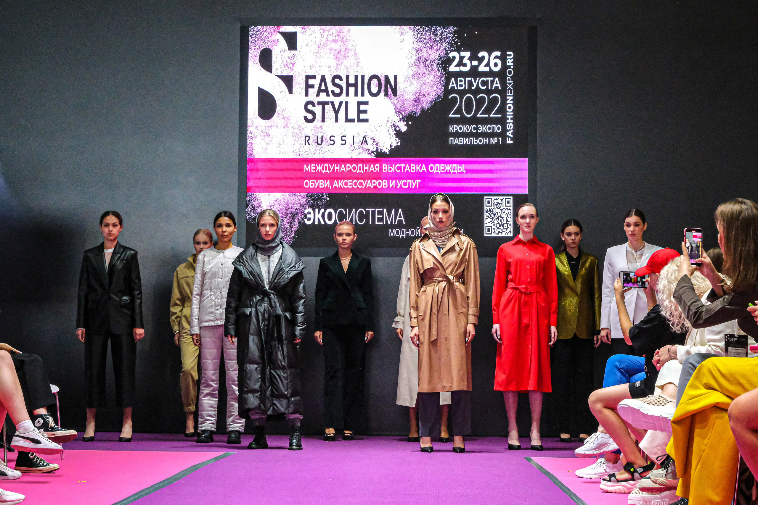  "Модели в ярких нарядах проходят по подиуму во время показа мод, освещенные яркими софитами и окруженные восторженными зрителями."