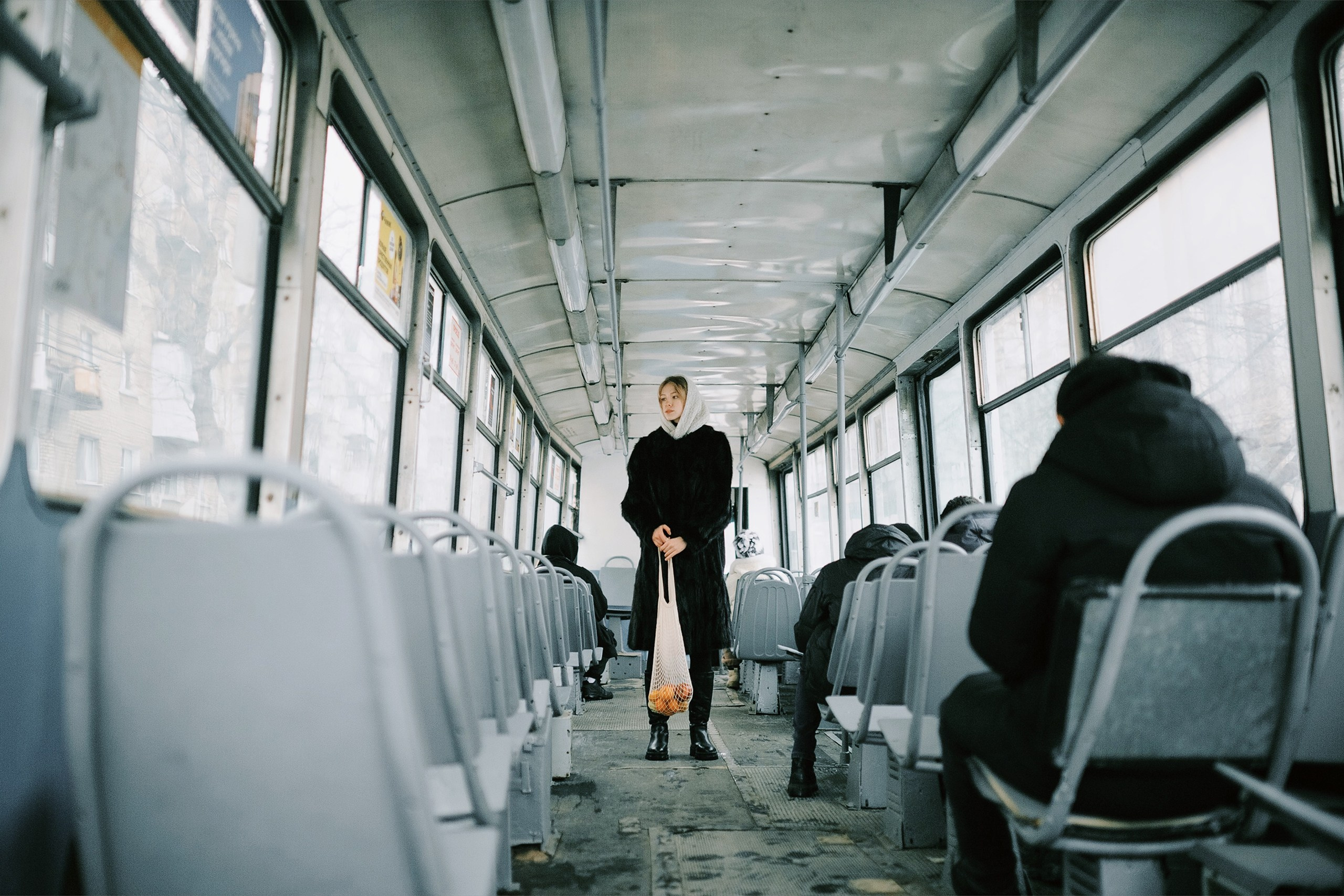 Девушка в шубе и белой шали с авоськой стоит в трамвае 