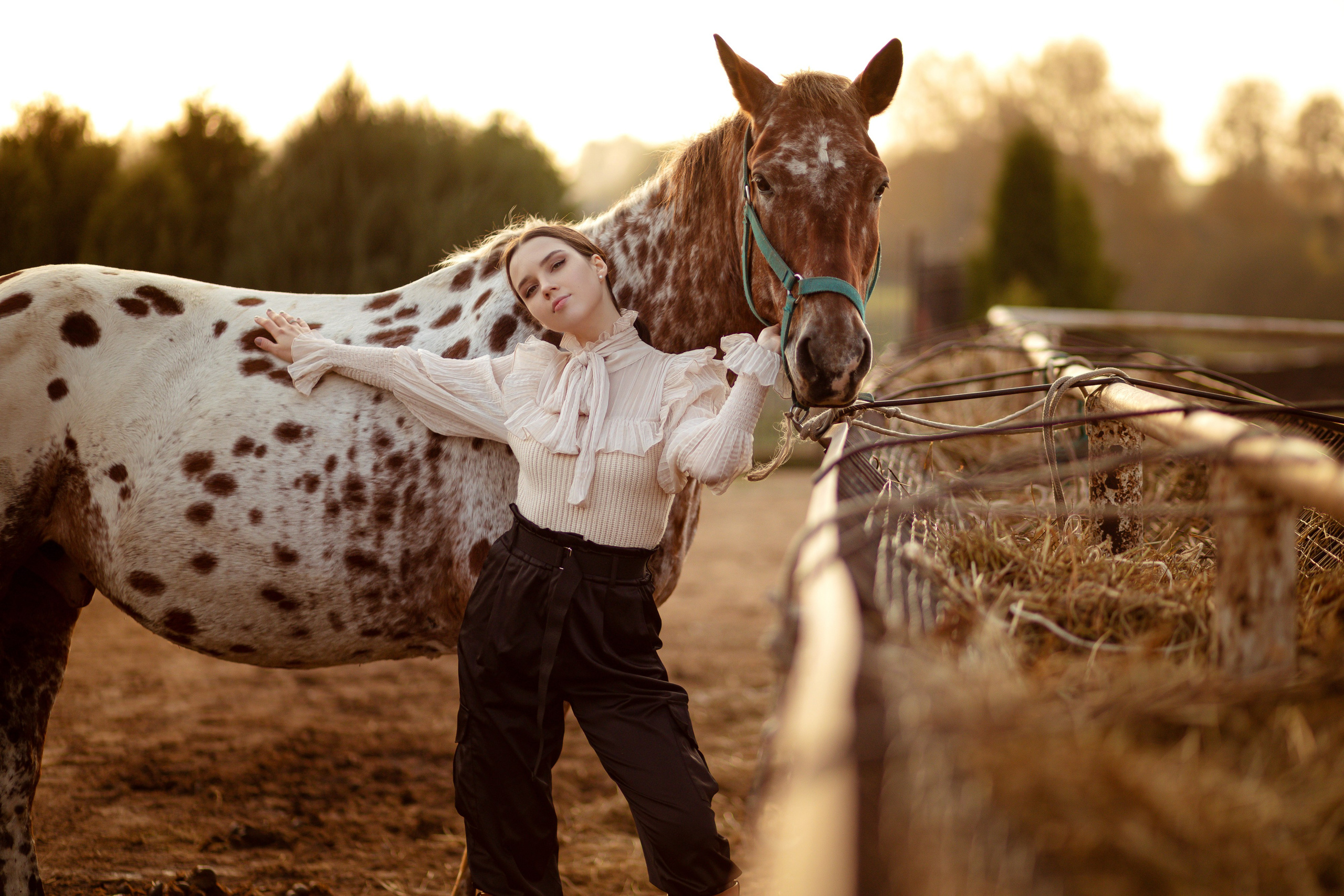 Девушка с лошадью стоит на фоне залитого солнцем леса.