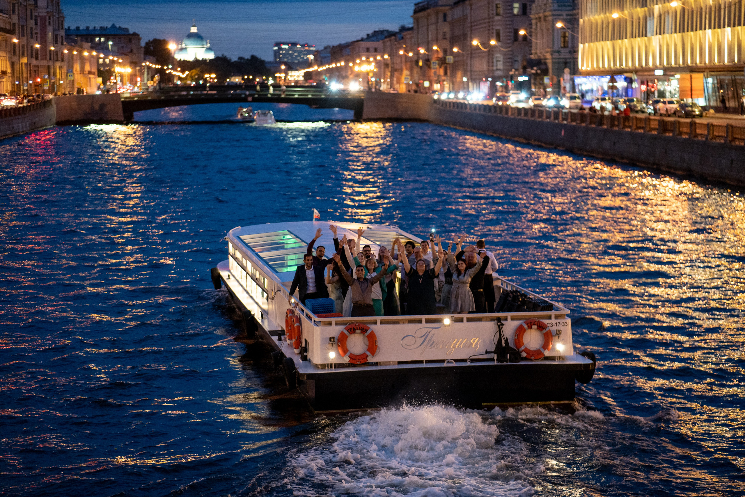 жених и невеста и гости стоят на яхте и машут рукой фотографа на уплывающем речном трамвайчике