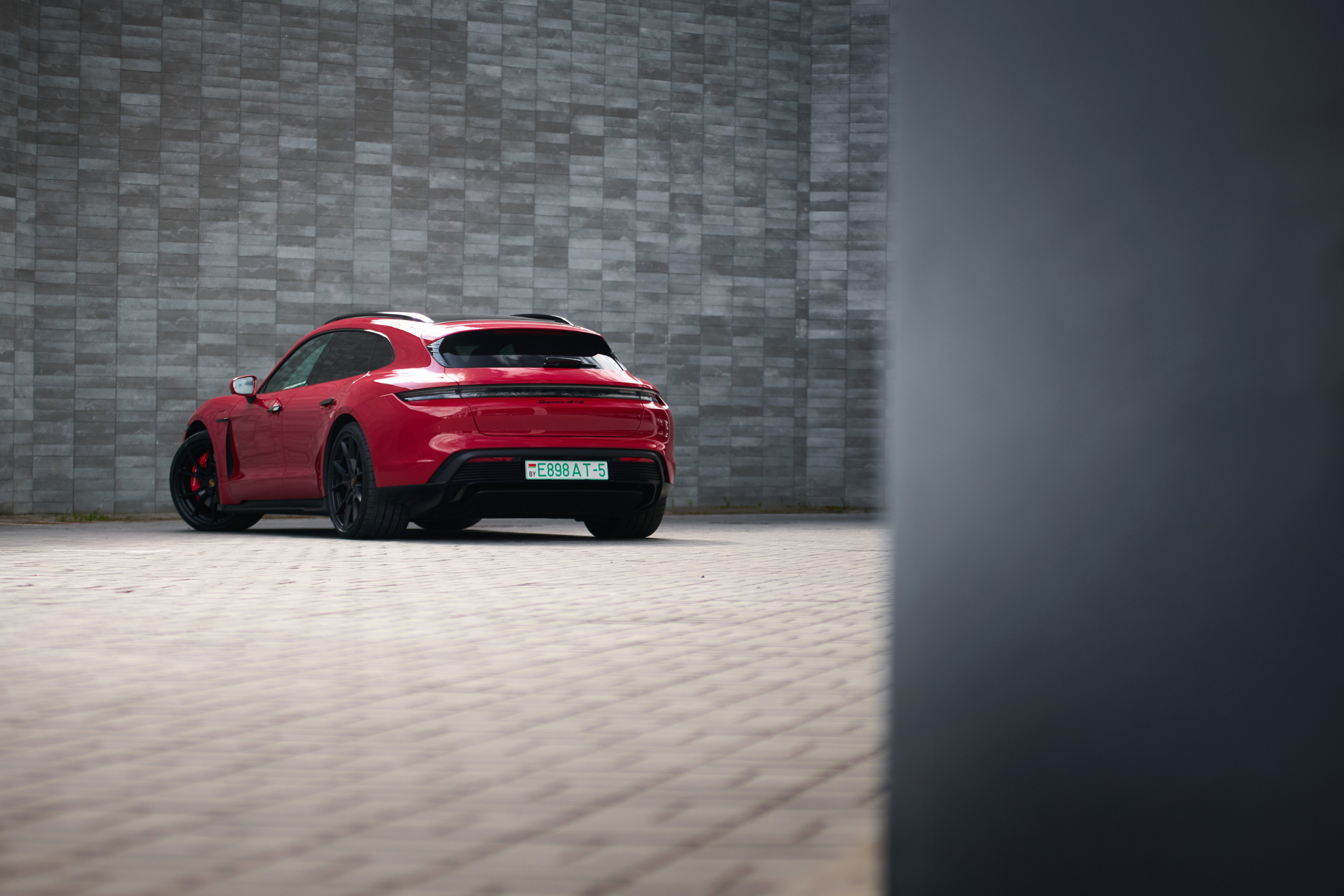 Красный Porsche Taycan GTS в дальнем плане на парковке у бетонной стены
