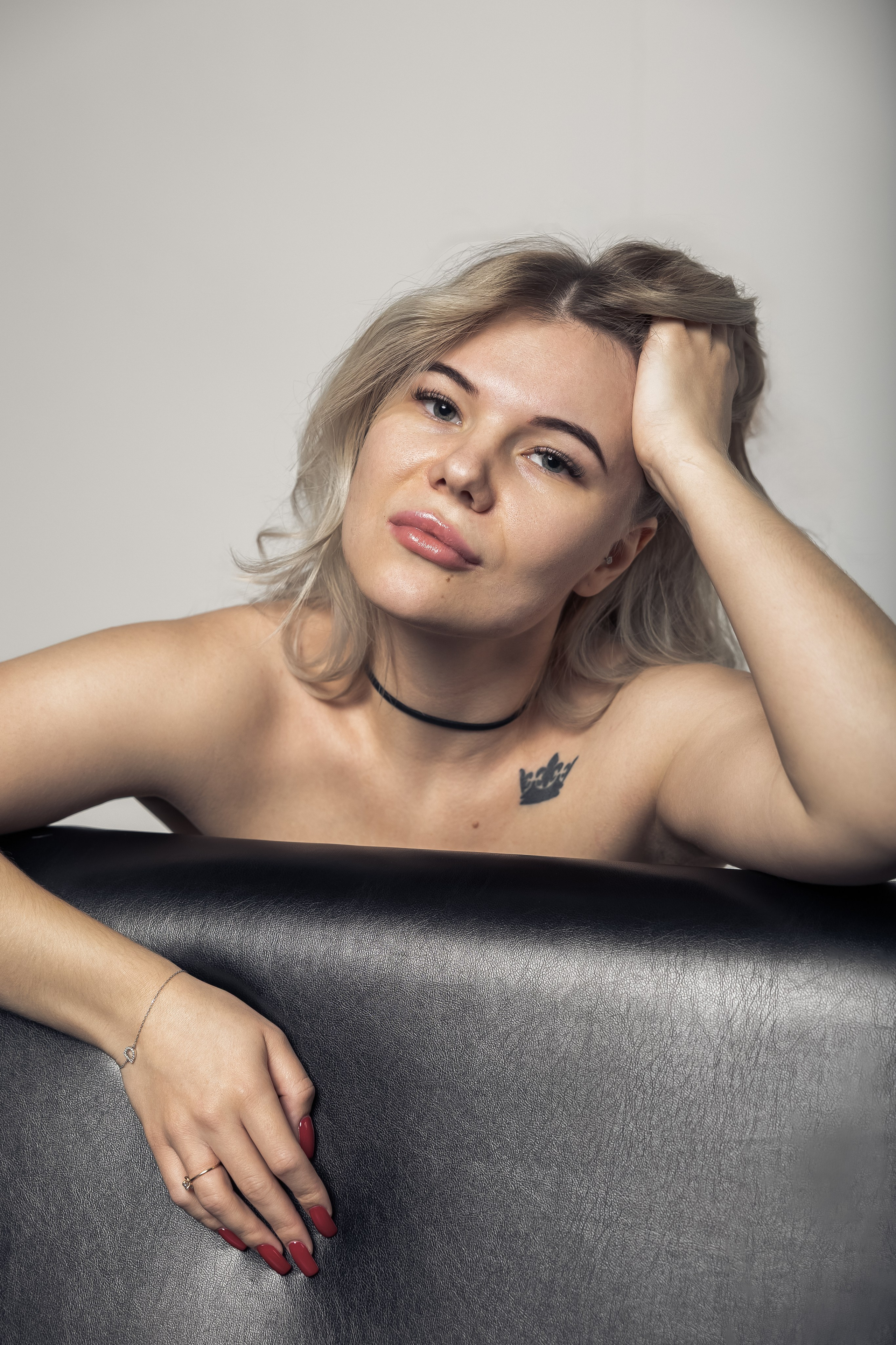 Девушка опирается на спинку кресла, расслабленная поза и задумчивый взгляд.