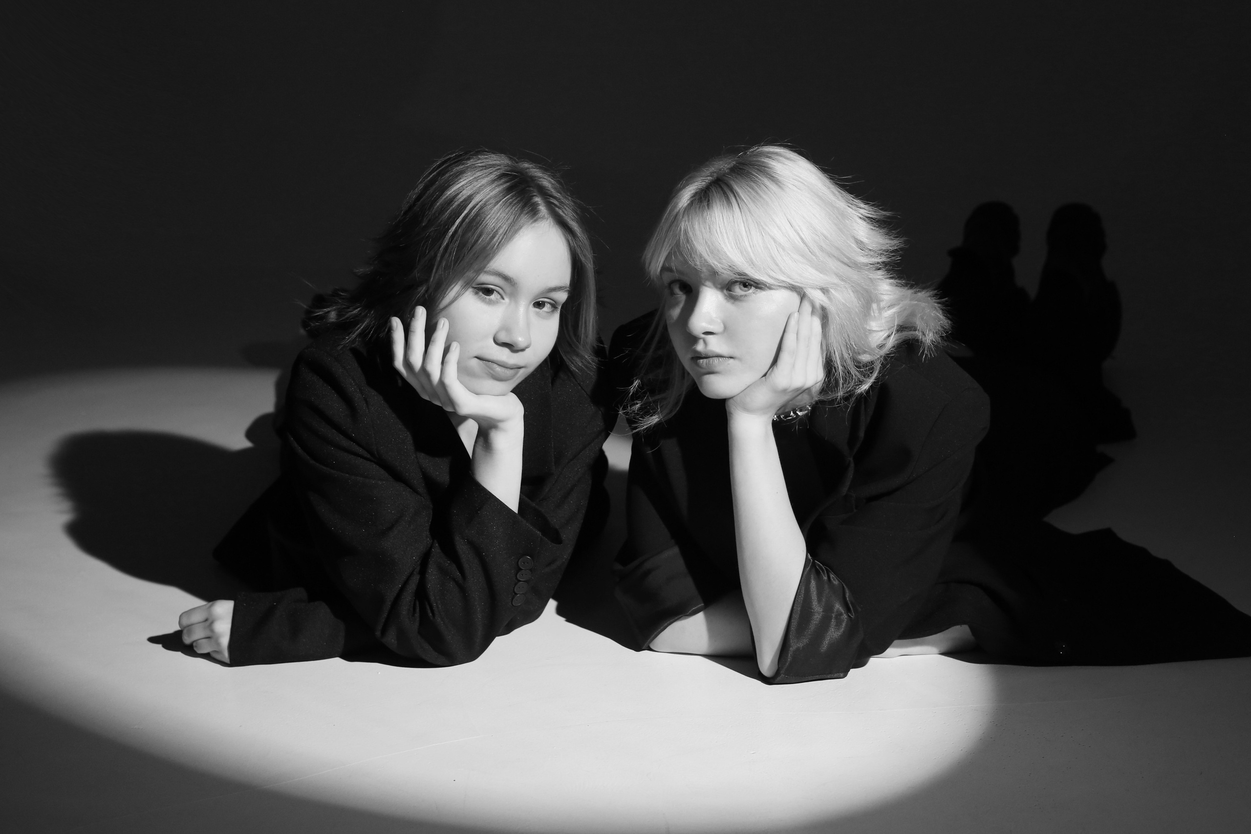 Студийная фотосессия «Геометрия»: две девушки в черных костюмах лежат на полу в круге света