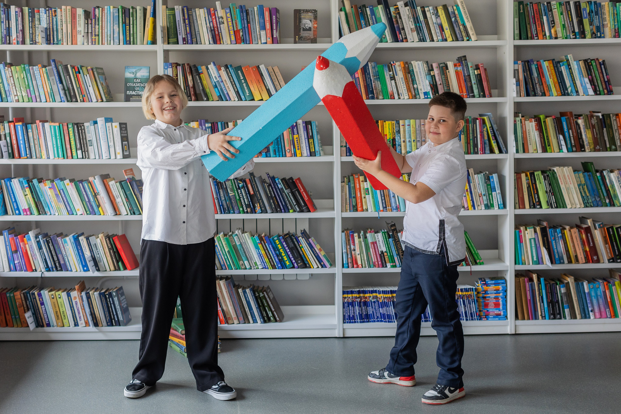 Два мальчика позируют с карандашами в библиотеке