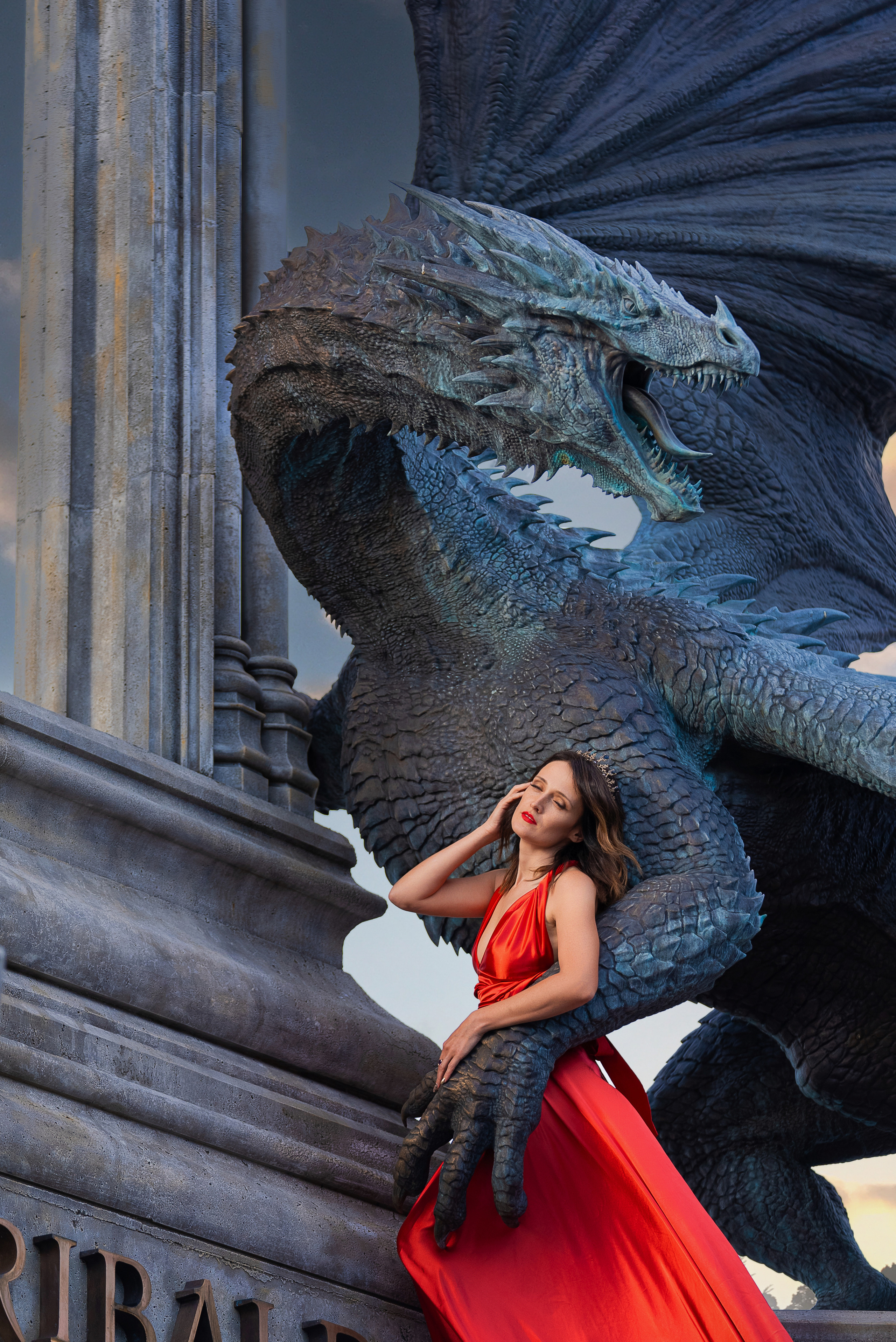 Девушка в алом наряде прикасается к шее огромного дракона, подчеркивая динамику и сказочность съёмки в готическом стиле.