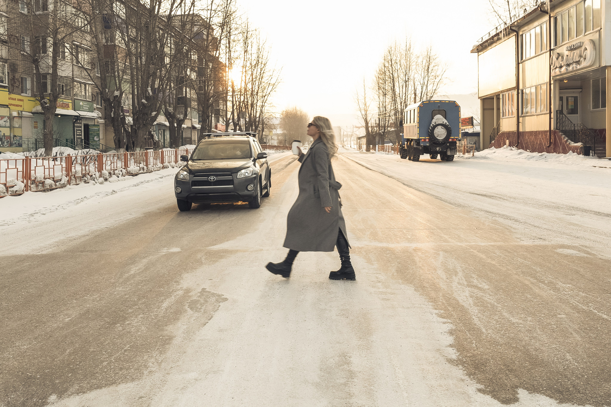 Девушка переходит зимнюю дорогу между машинами — уличный кадр.