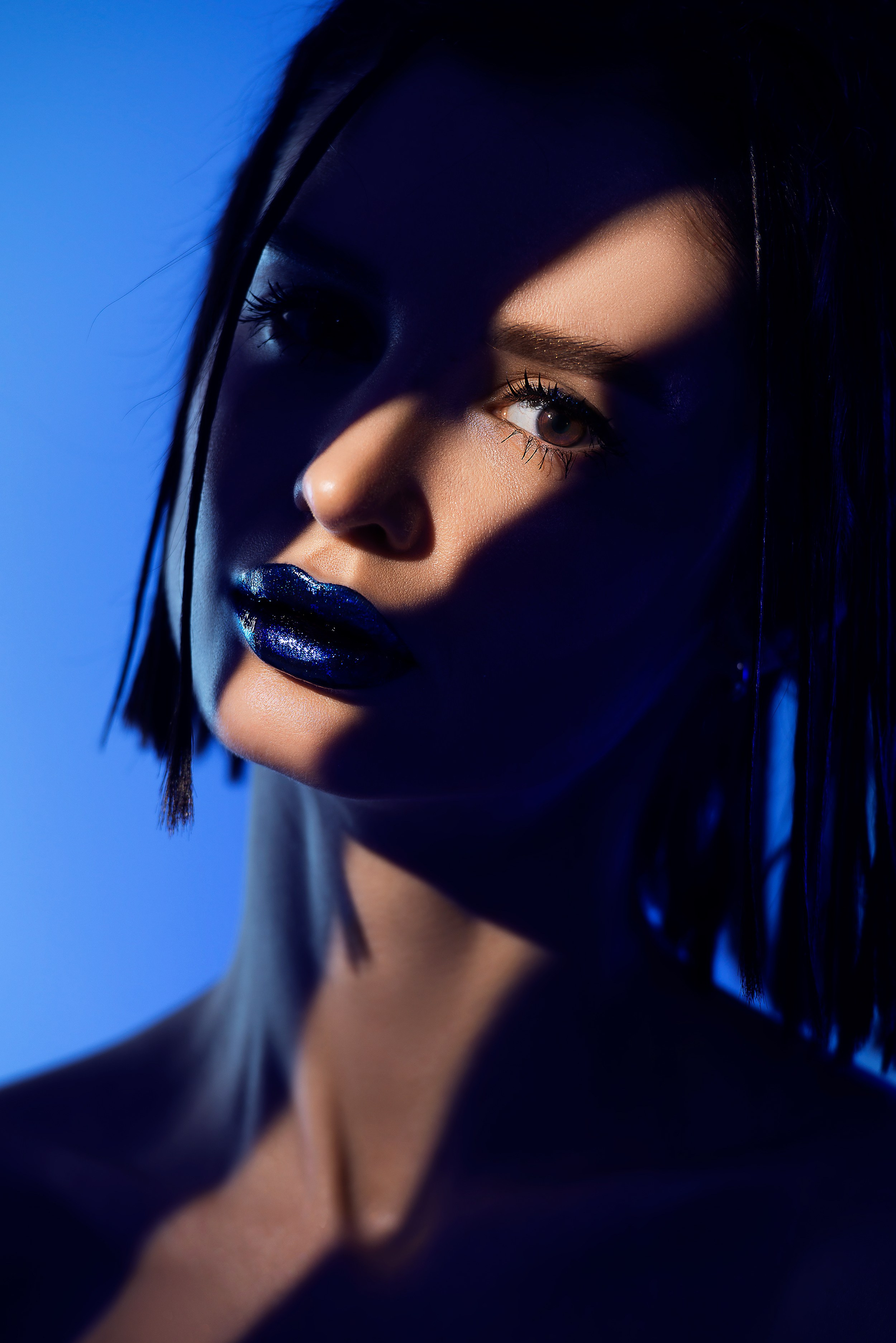 Арт портрет девушки на синем фоне. По лицу проходит полоса света, выделяя яркие синие губы
