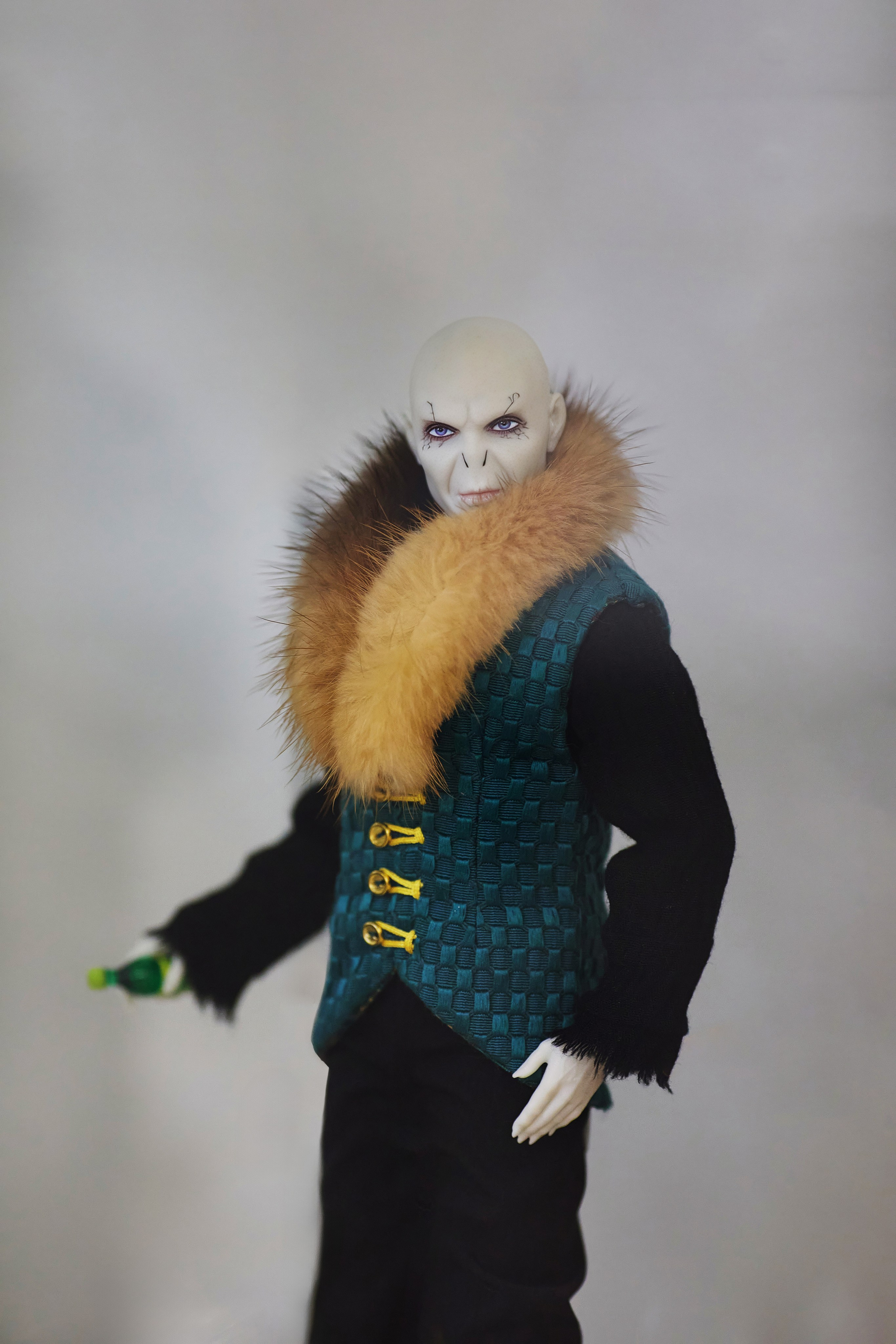 Кукла, изображающая Волан-де-Морта, одетого в тёмно-зелёный жилет с золотыми застёжками и коричневым меховым воротником