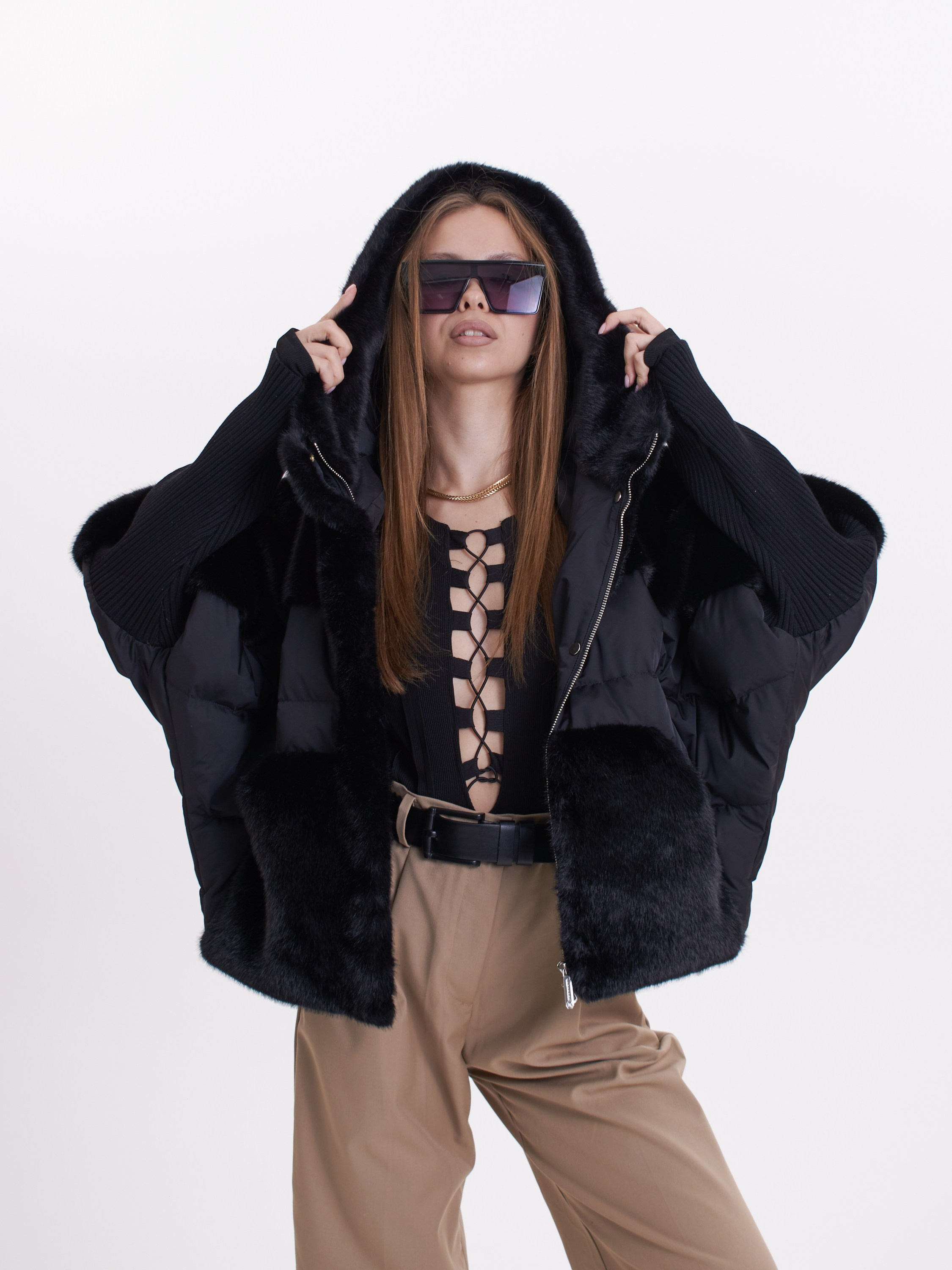 Девушка в шубе, бежевых штанах и темных очках позирует на светлом фоне