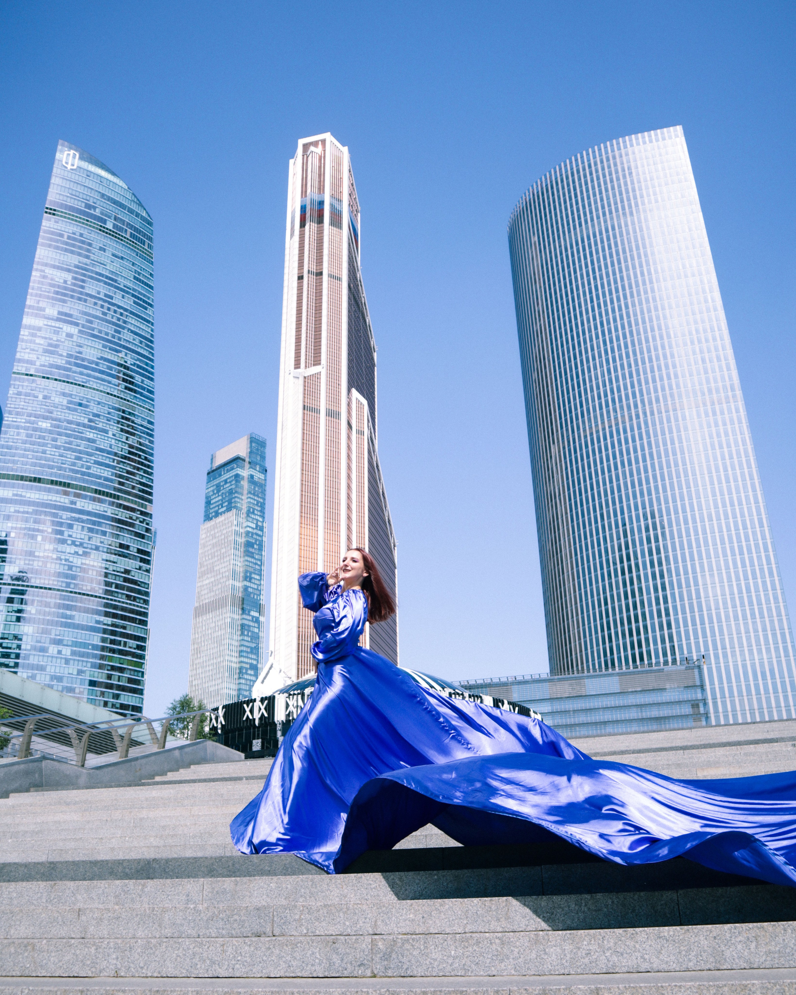 женщина в синем платье со шлейфом на фоне небоскребов