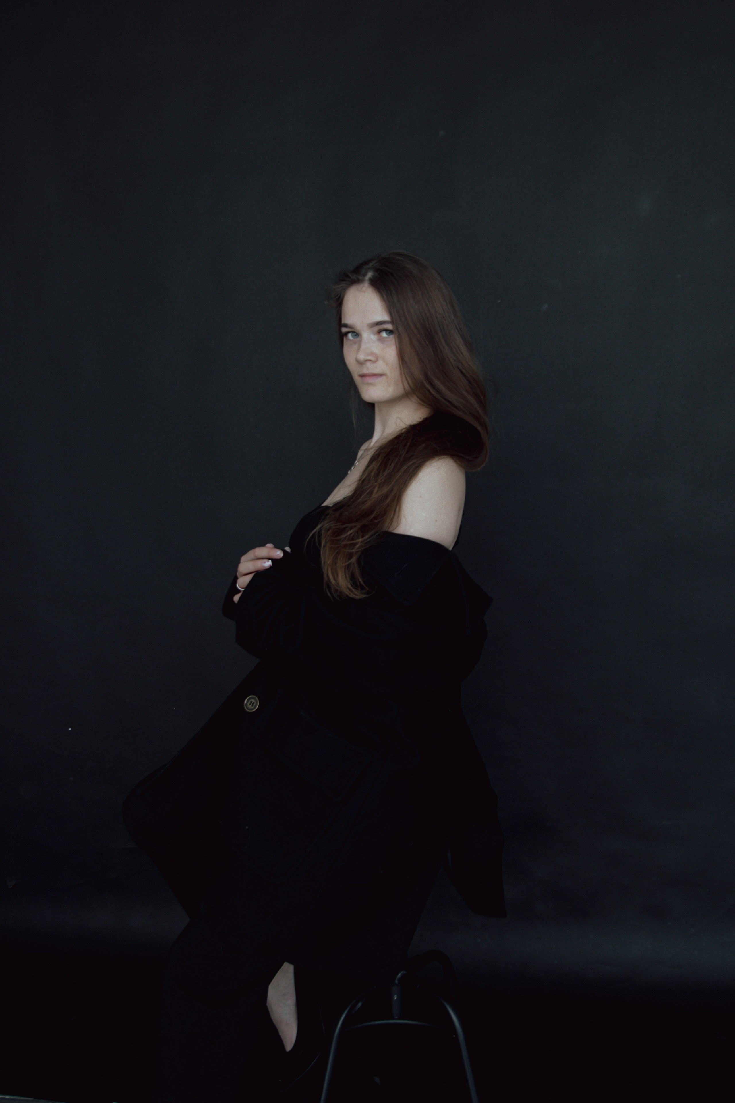 девушка сидит в пальто на  стуле на черном фоне с распущенными волосами