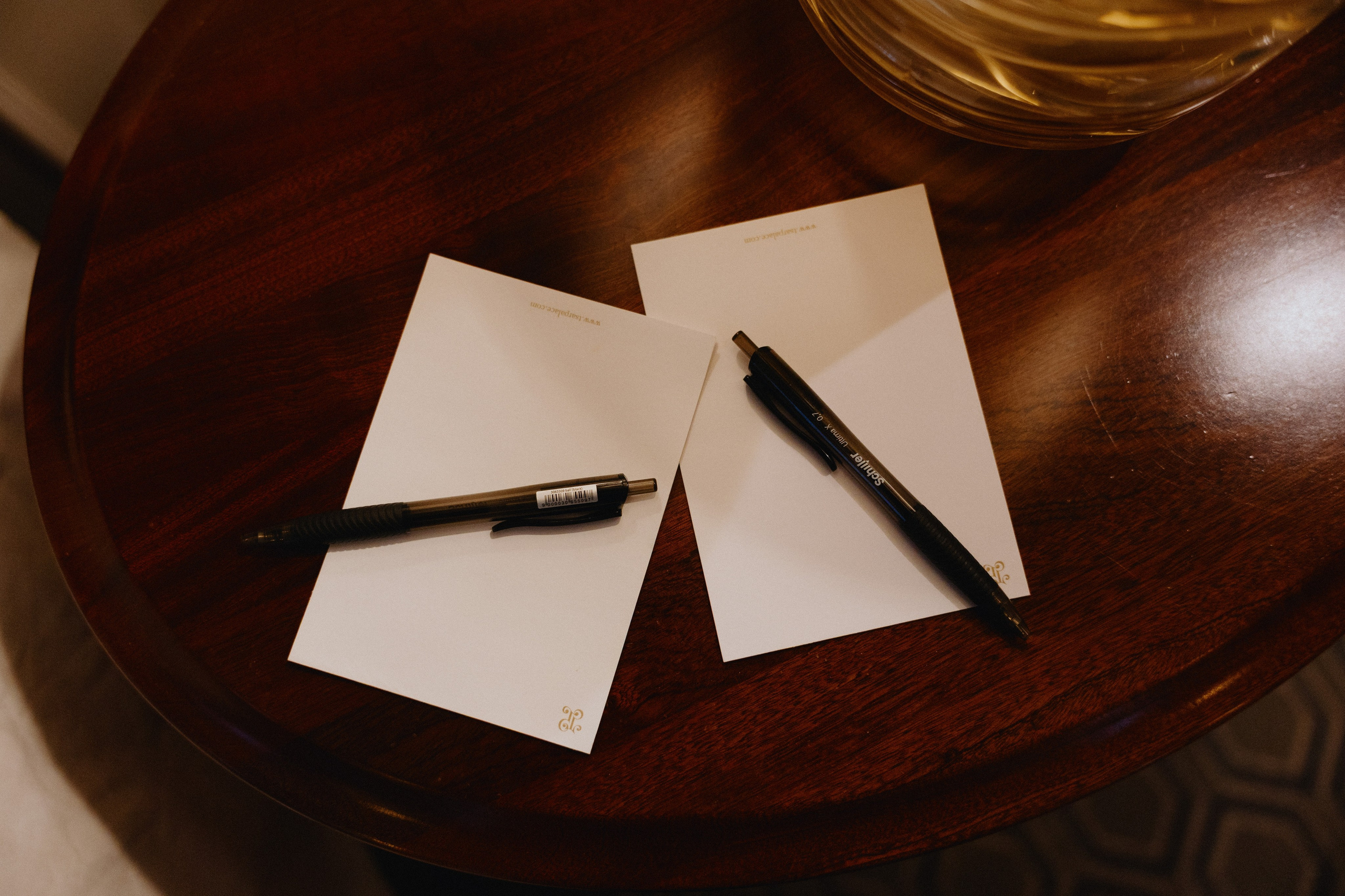 Две открытки и две ручки лежат на круглом деревянном столе.