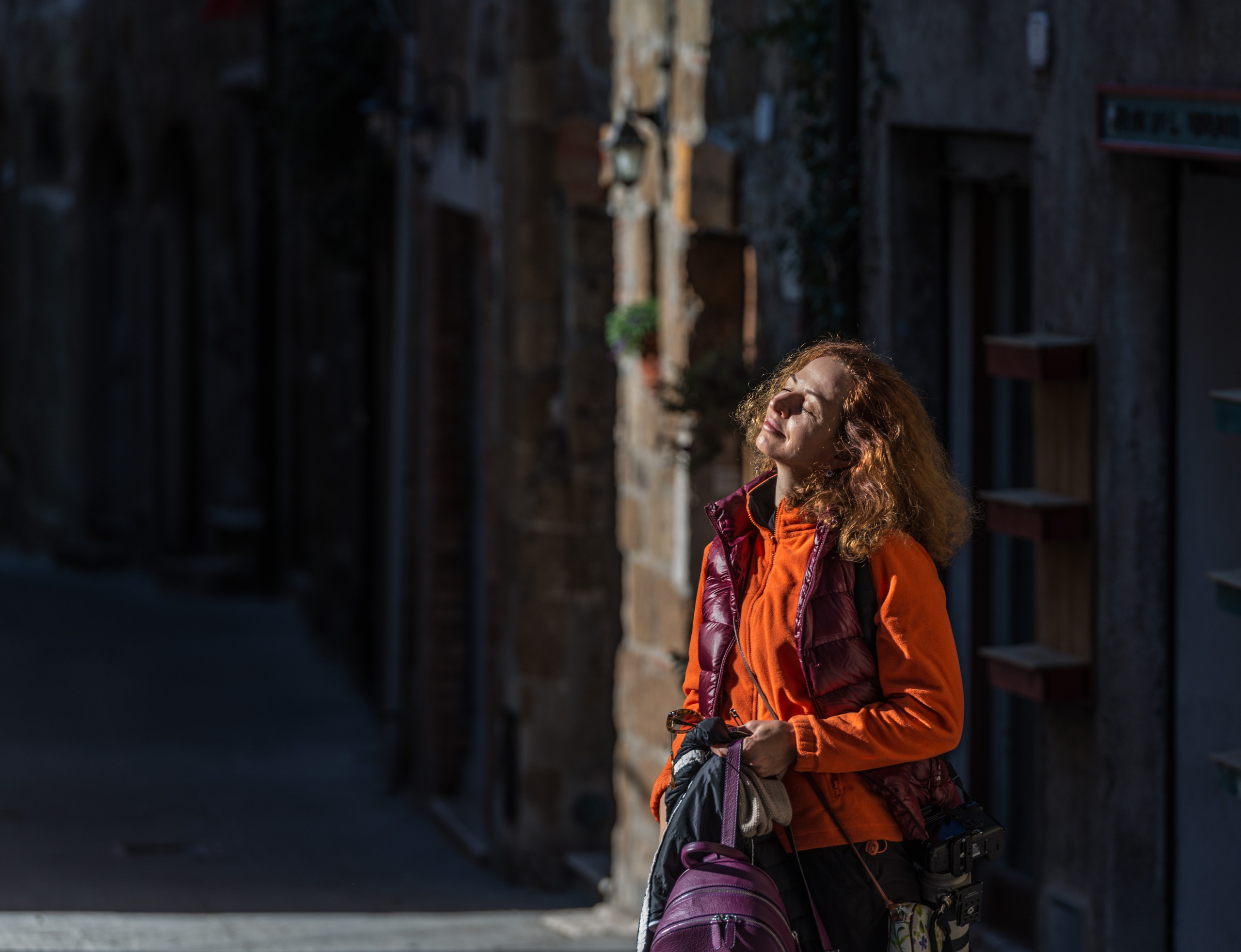 портрет женщины в оранжевом жилете, наслаждающейся солнцем в узком итальянском переулке: фотопрогулка
